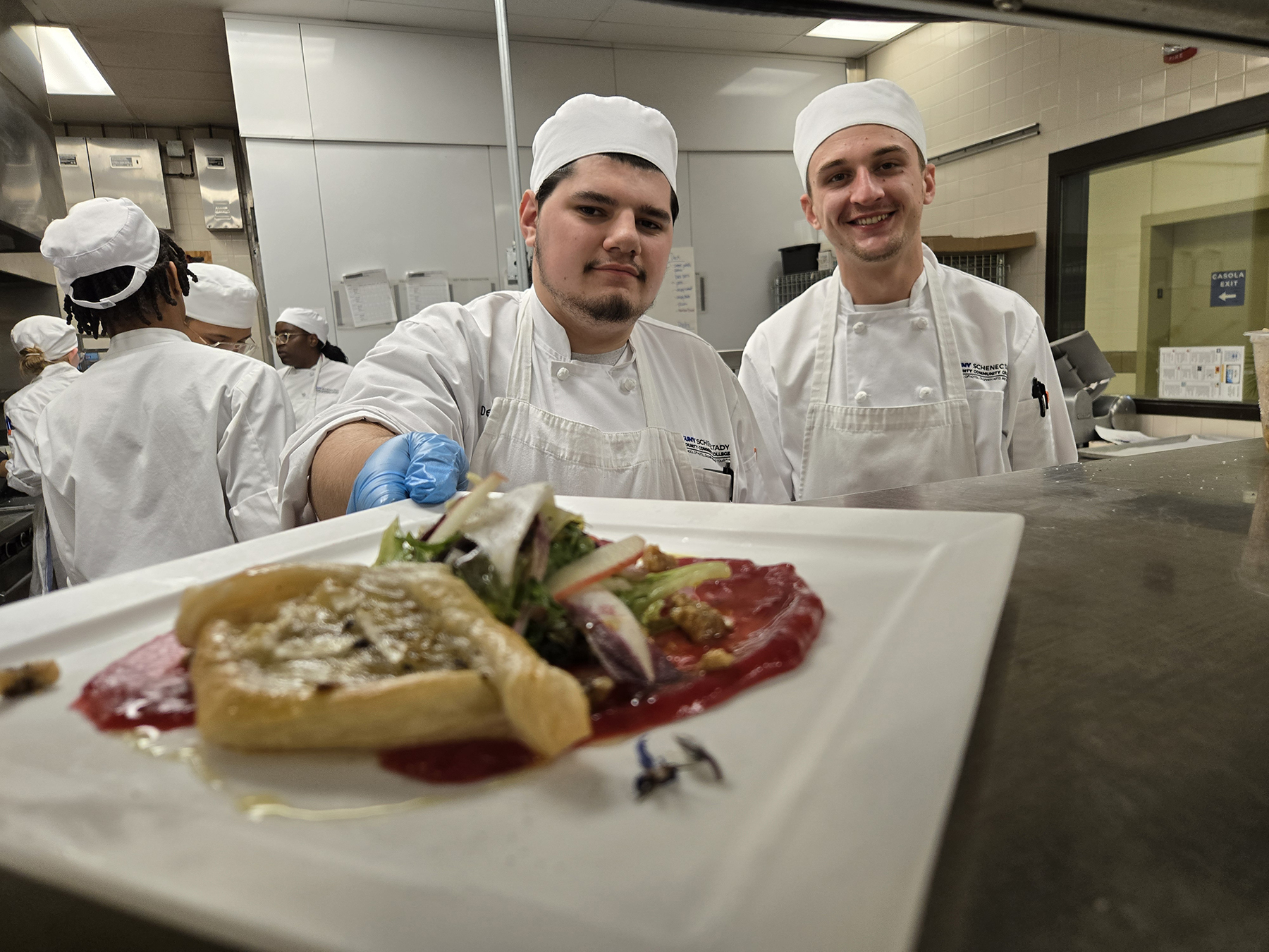 Student chefs holding plate of food in kitchen