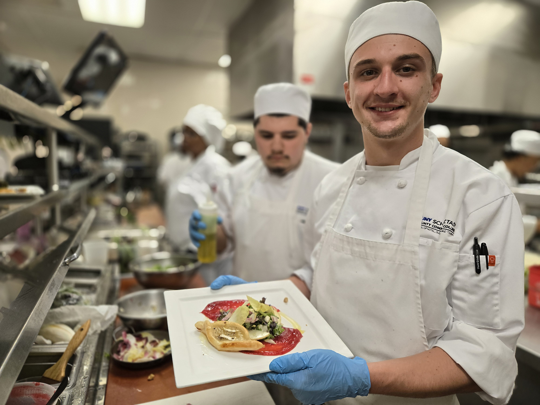 Student chef holding plate of food inside kitchen