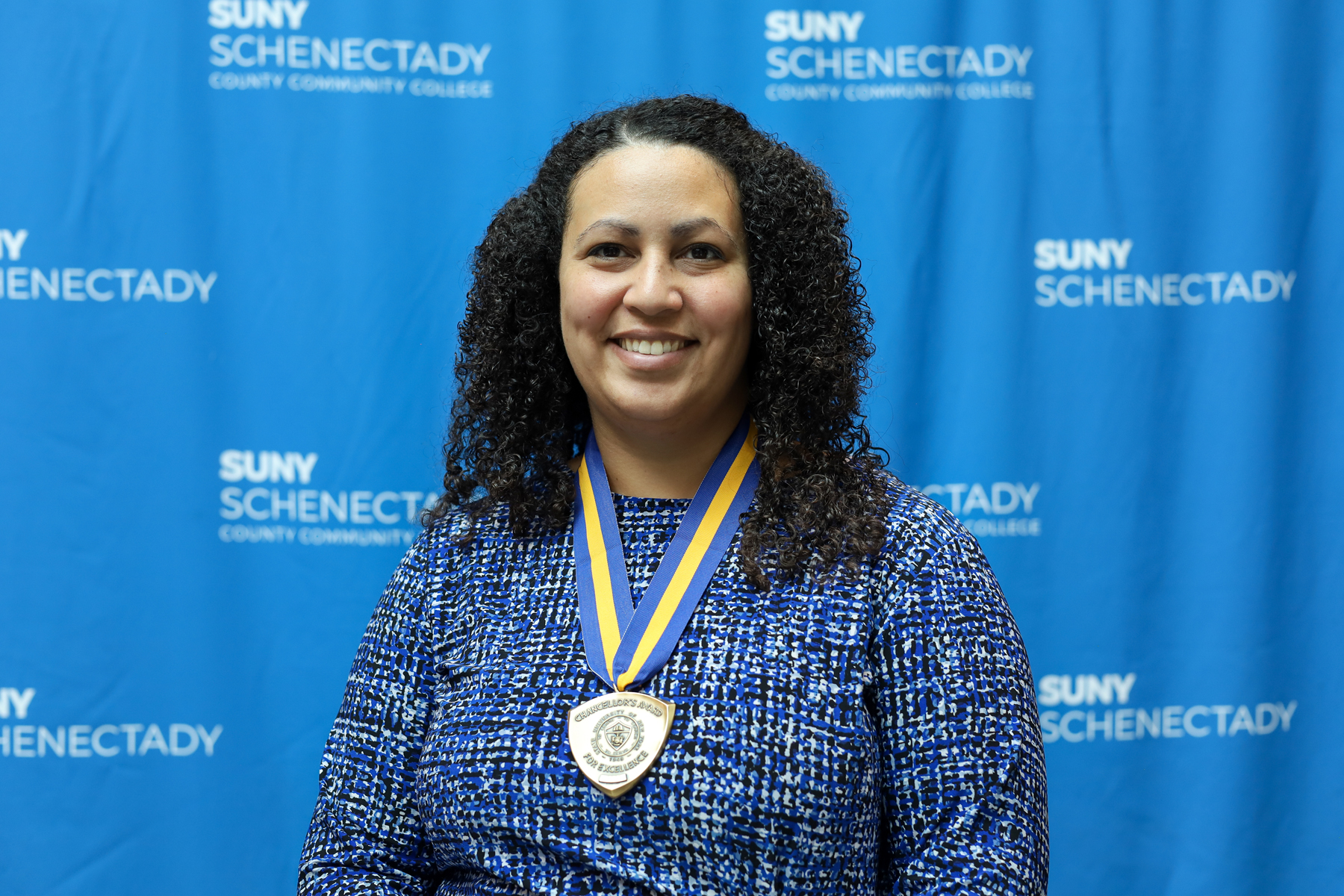 Catia Laird de Polanco wearing award medallion in front of College backdrop, smiling