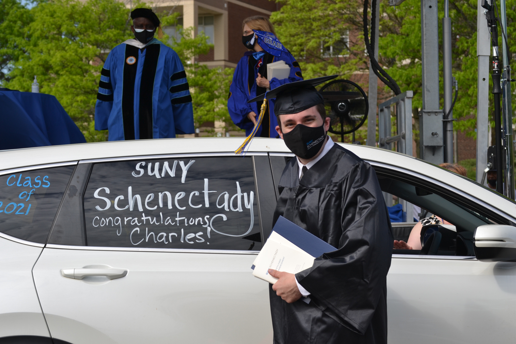 Charles, a graduate, in cap and gown near car.