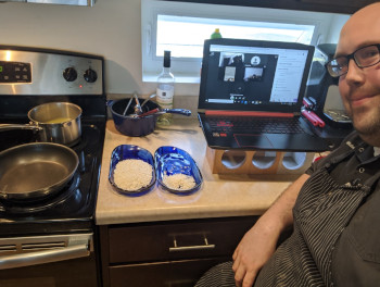 Chef Michael Stamets seated at counter in his home kitchen with pans and laptop