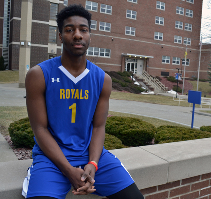 Photo of Christian Corker in basketball uniform sitting outside building on campus