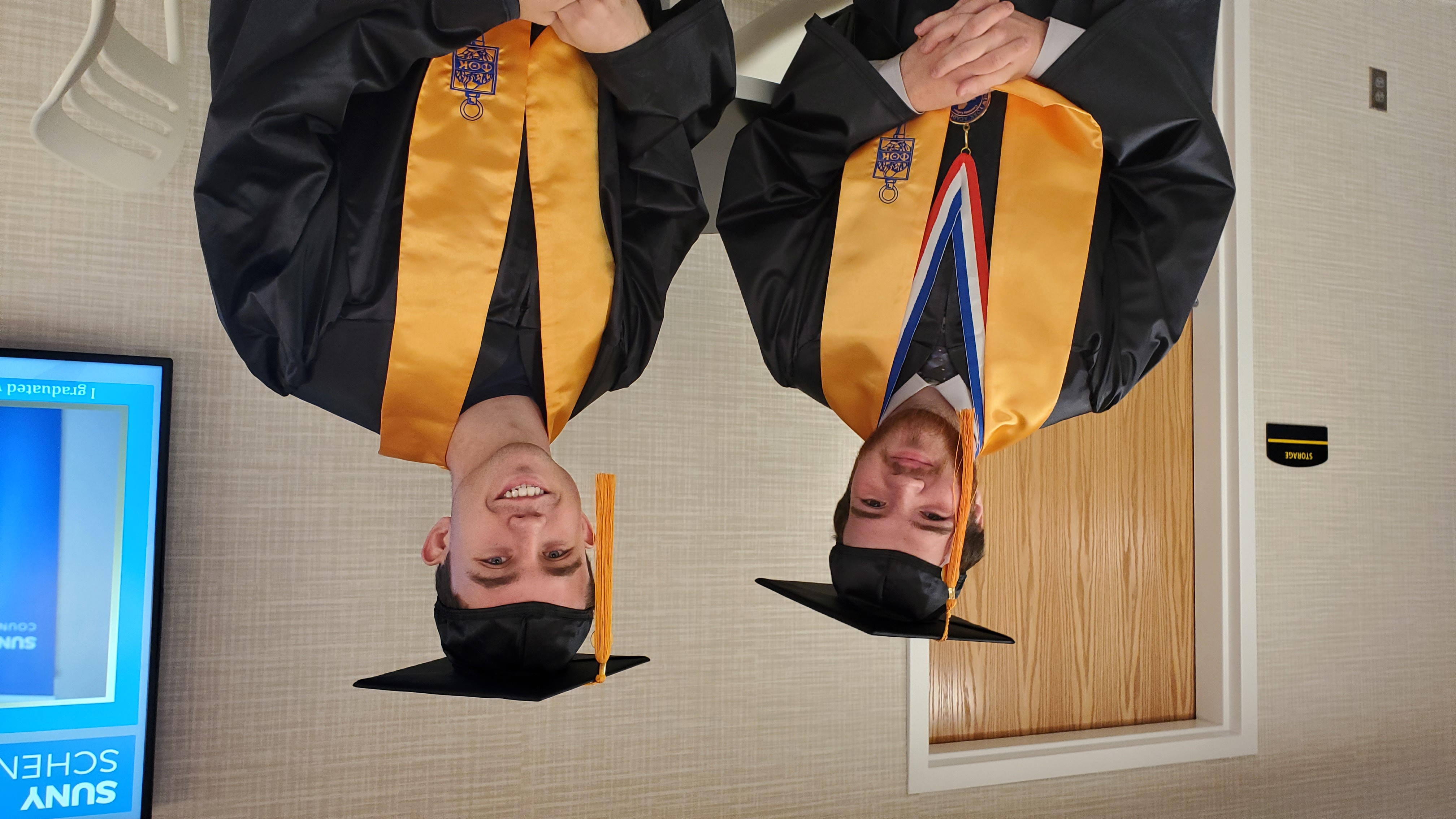 Two male students in regalia seated inside Learning Commons