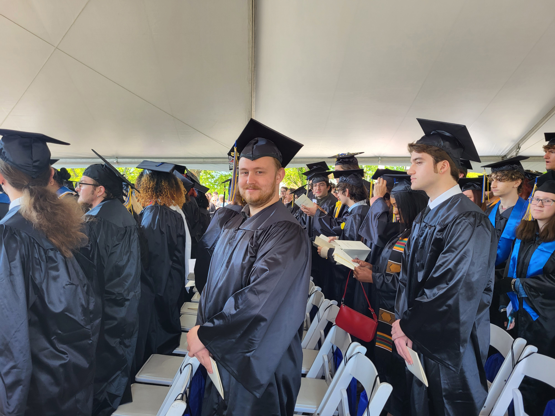 Graduate sitting in row under tent with other grads, smiling