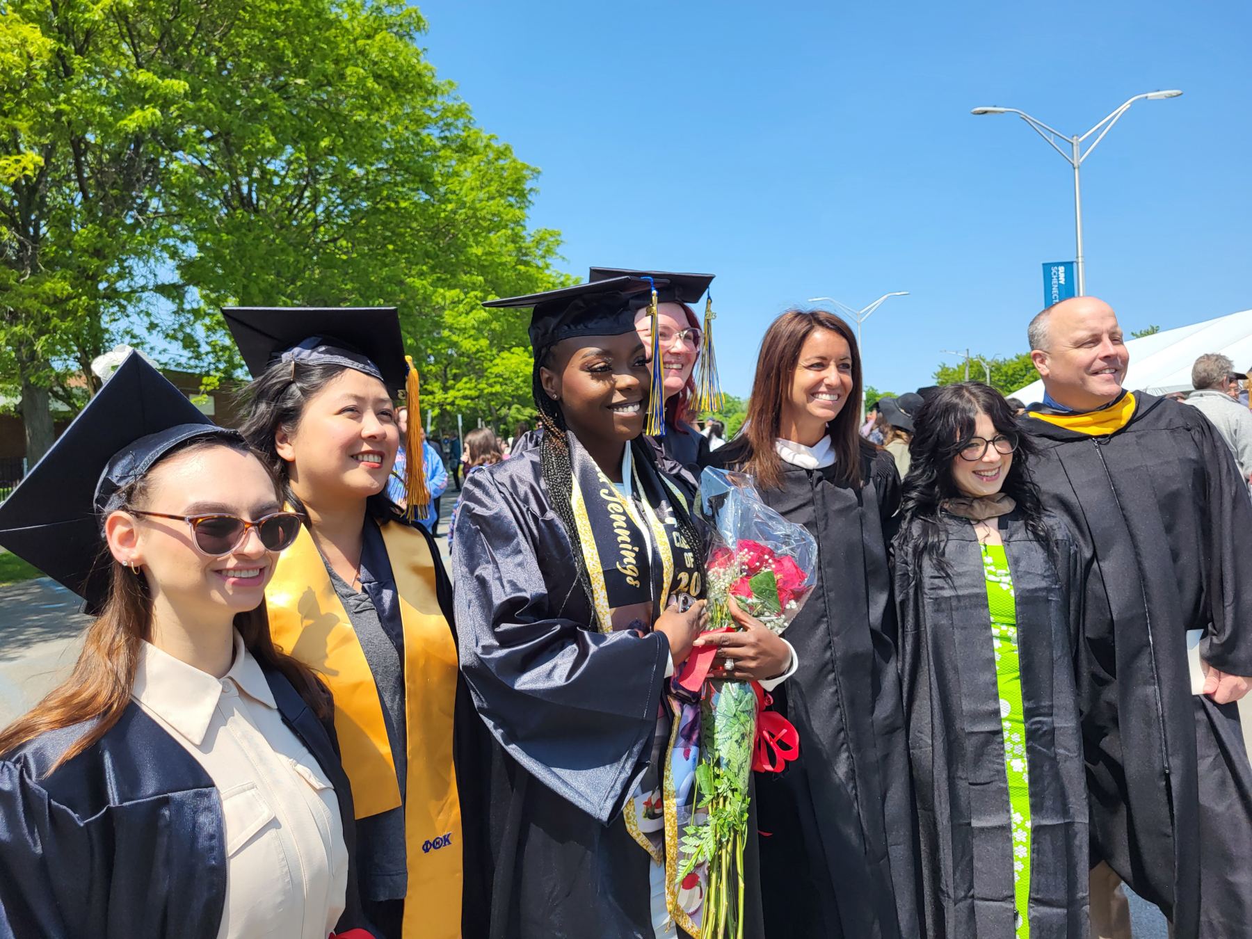 Graduates and faculty standing outside, posing, smiling for photo