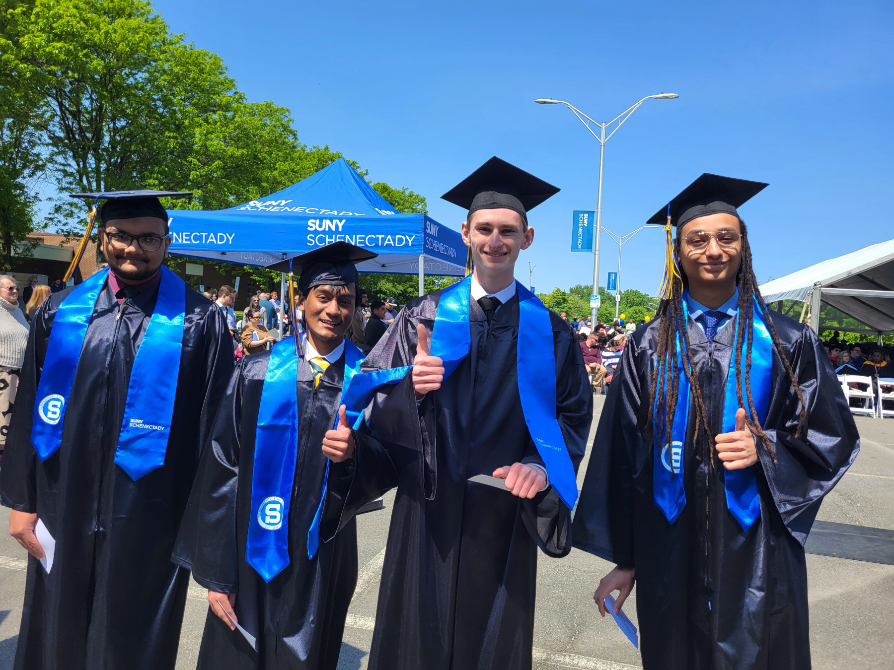 Four graduates, thumbs up, smiling before walking on stage