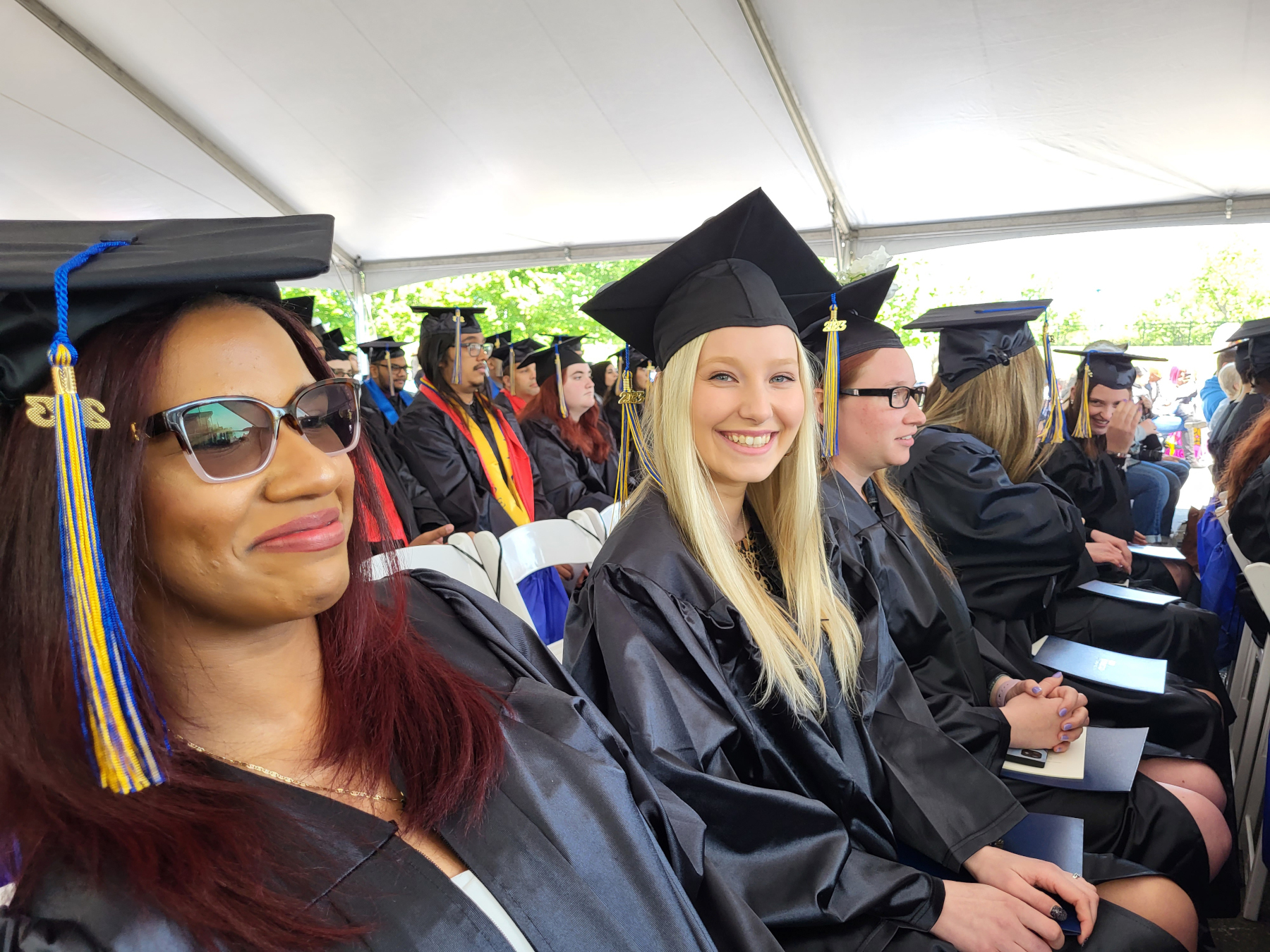 Graduates smiling, seated under tent outside