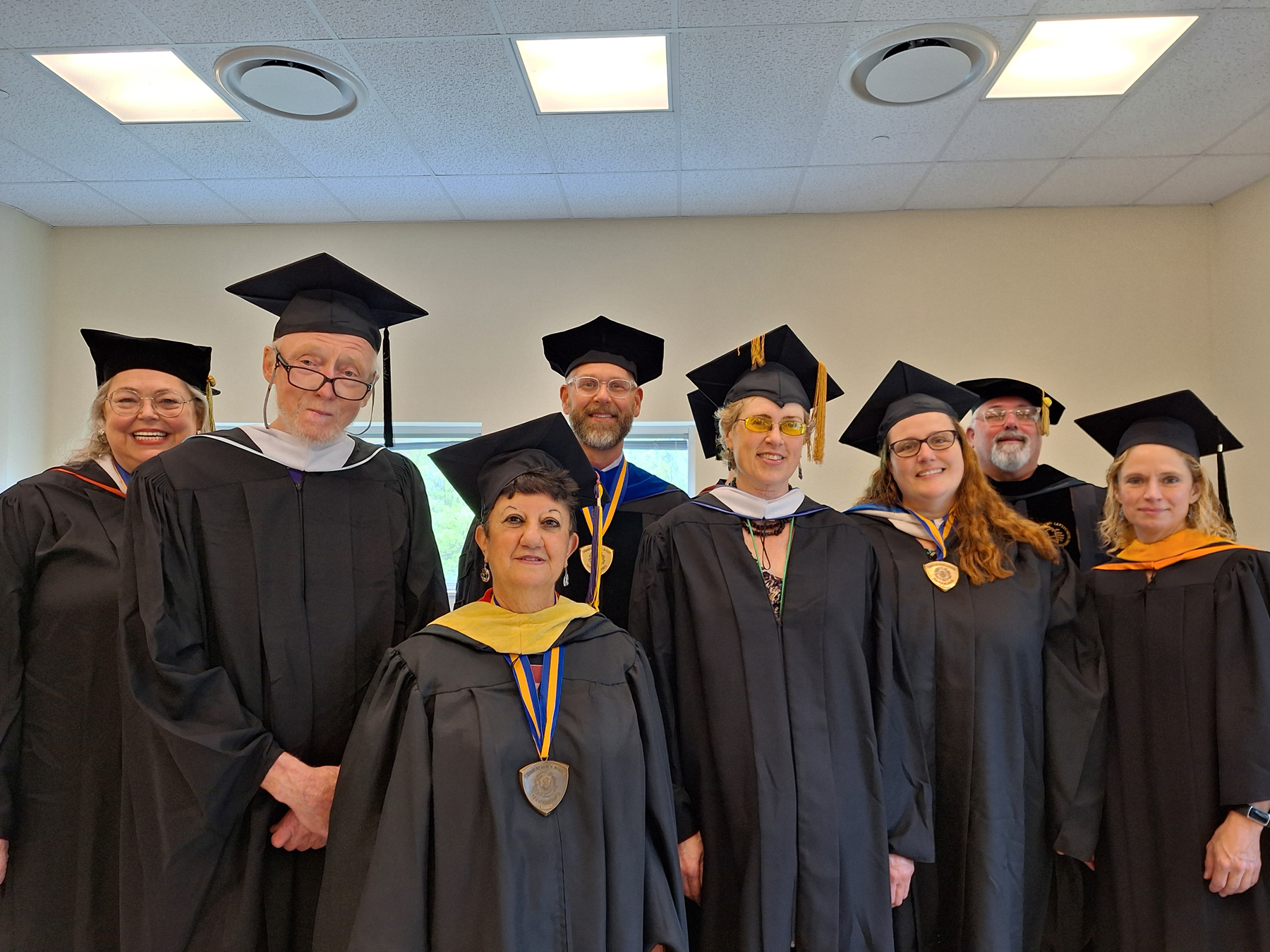 Liberal Arts faculty in caps and gowns, standing inside, smiling