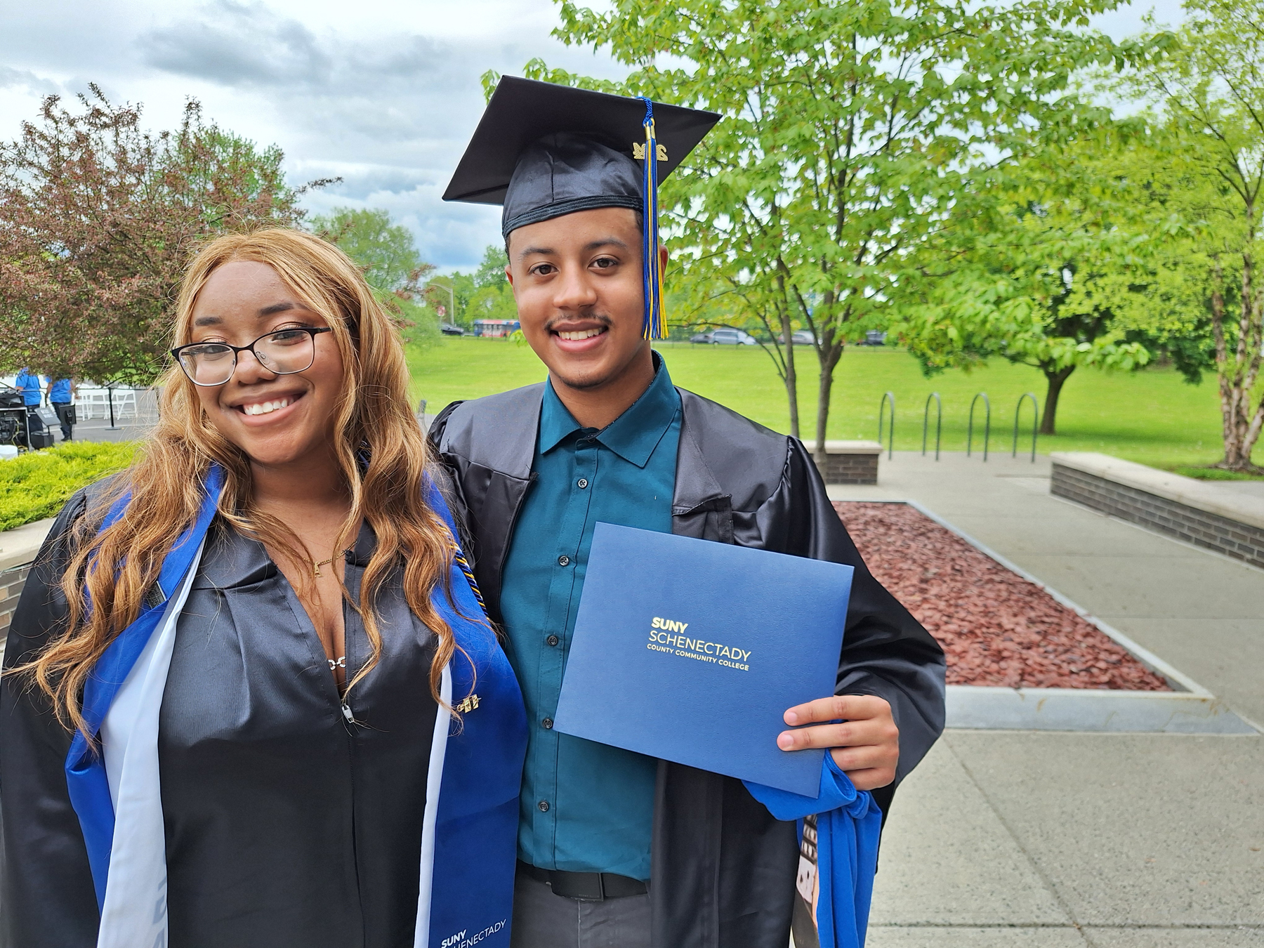 Two graduates holding diplomas outside, smiling