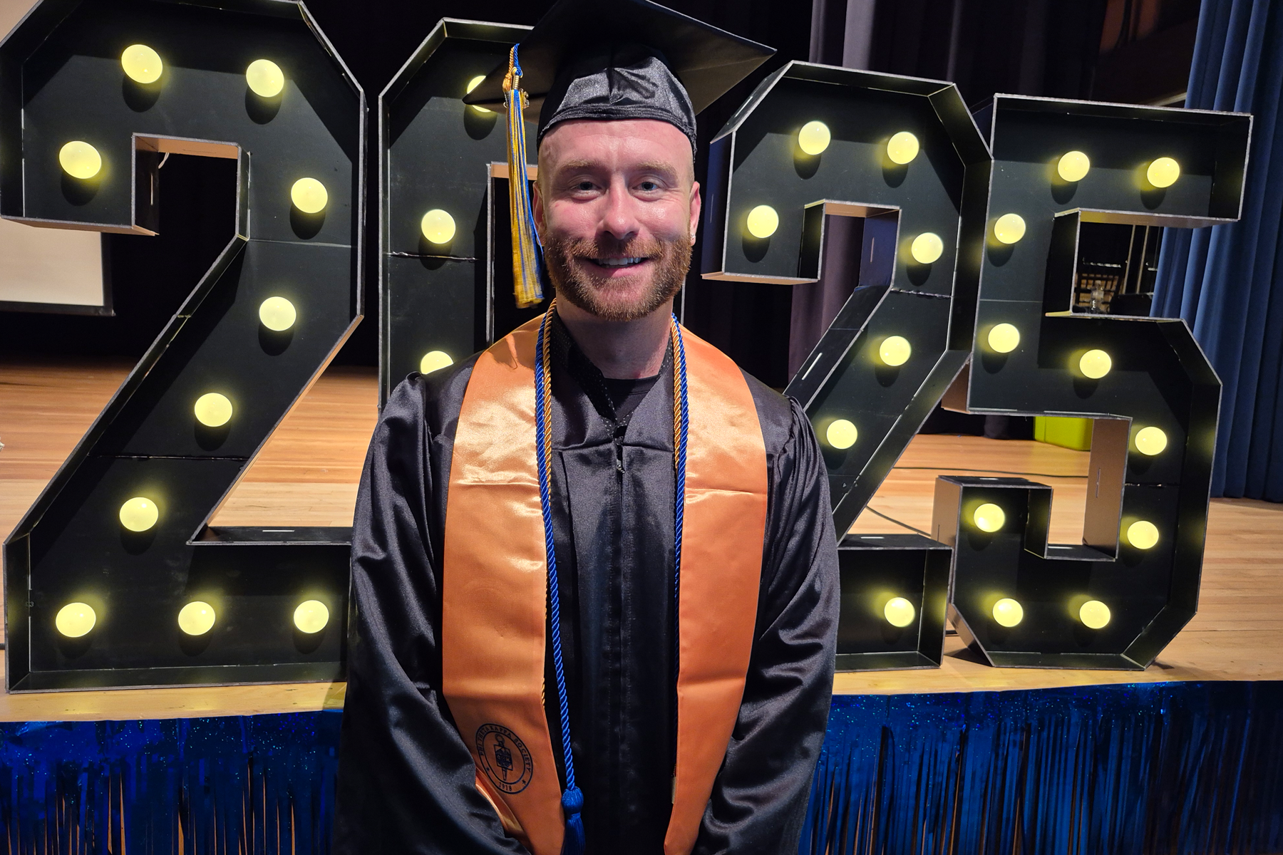 Graduate standing in front of 2025 neon sign