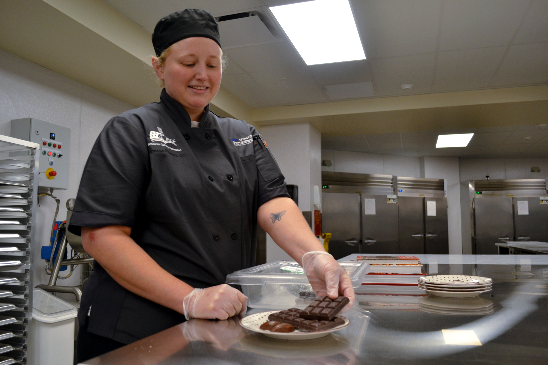 Vanessa Traver in new Confections Lab displaying finished chocolate bars on plate.
