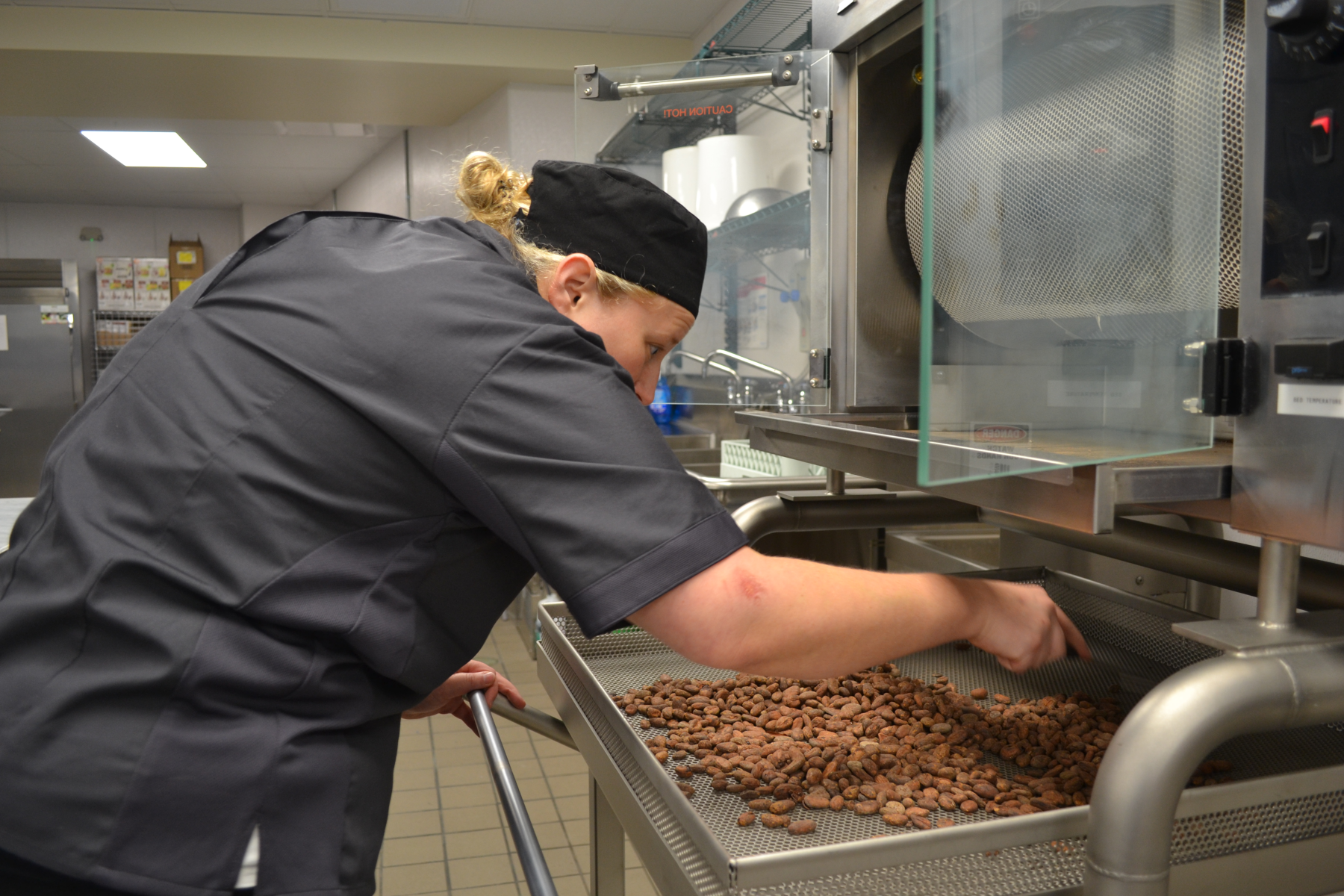 Vanessa Traver in new Confections Lab putting cocoa beans into equipment.
