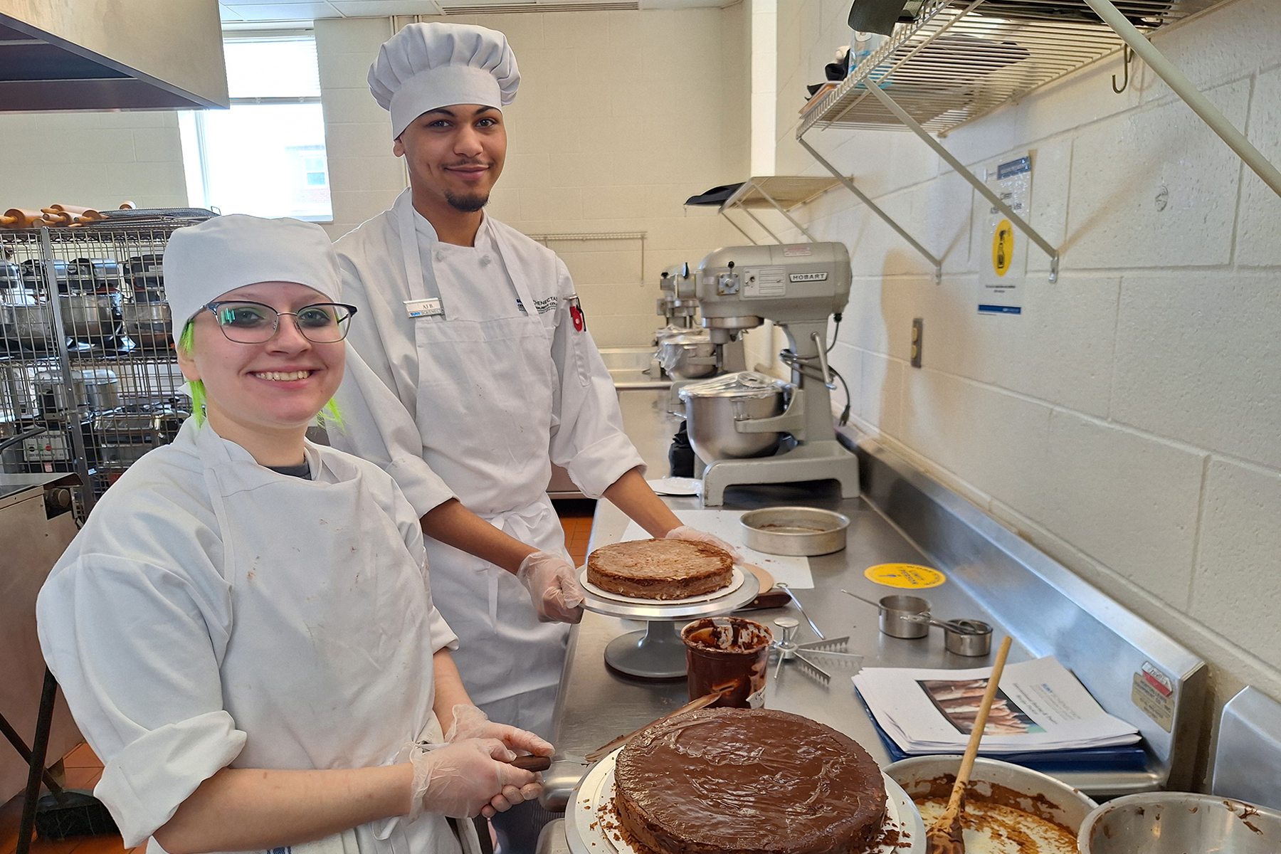 Two students in uniform making chocolate cake in baking lab