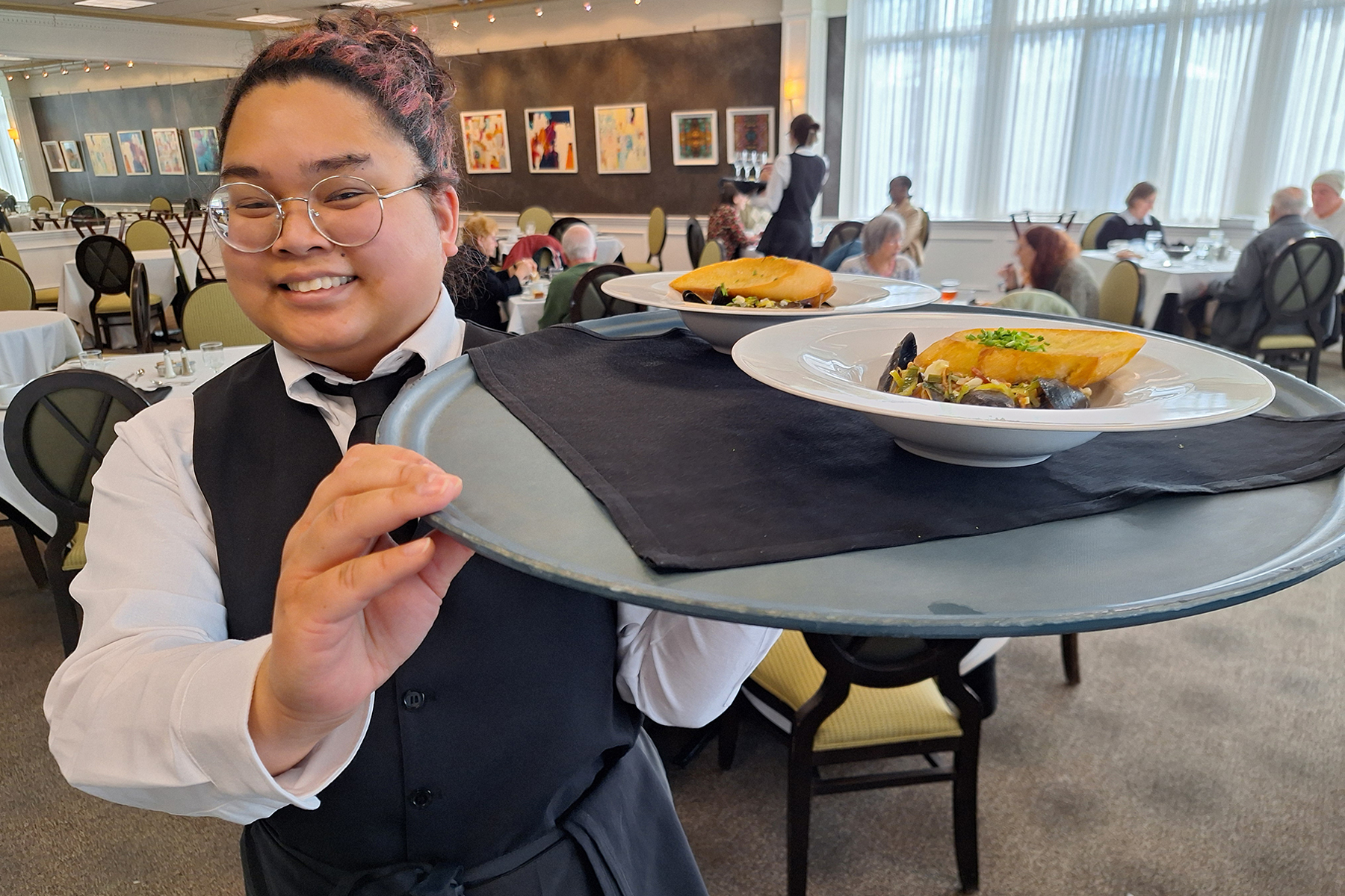 Student in hospitality uniform, holding tray with food on it in Casola Dining Room