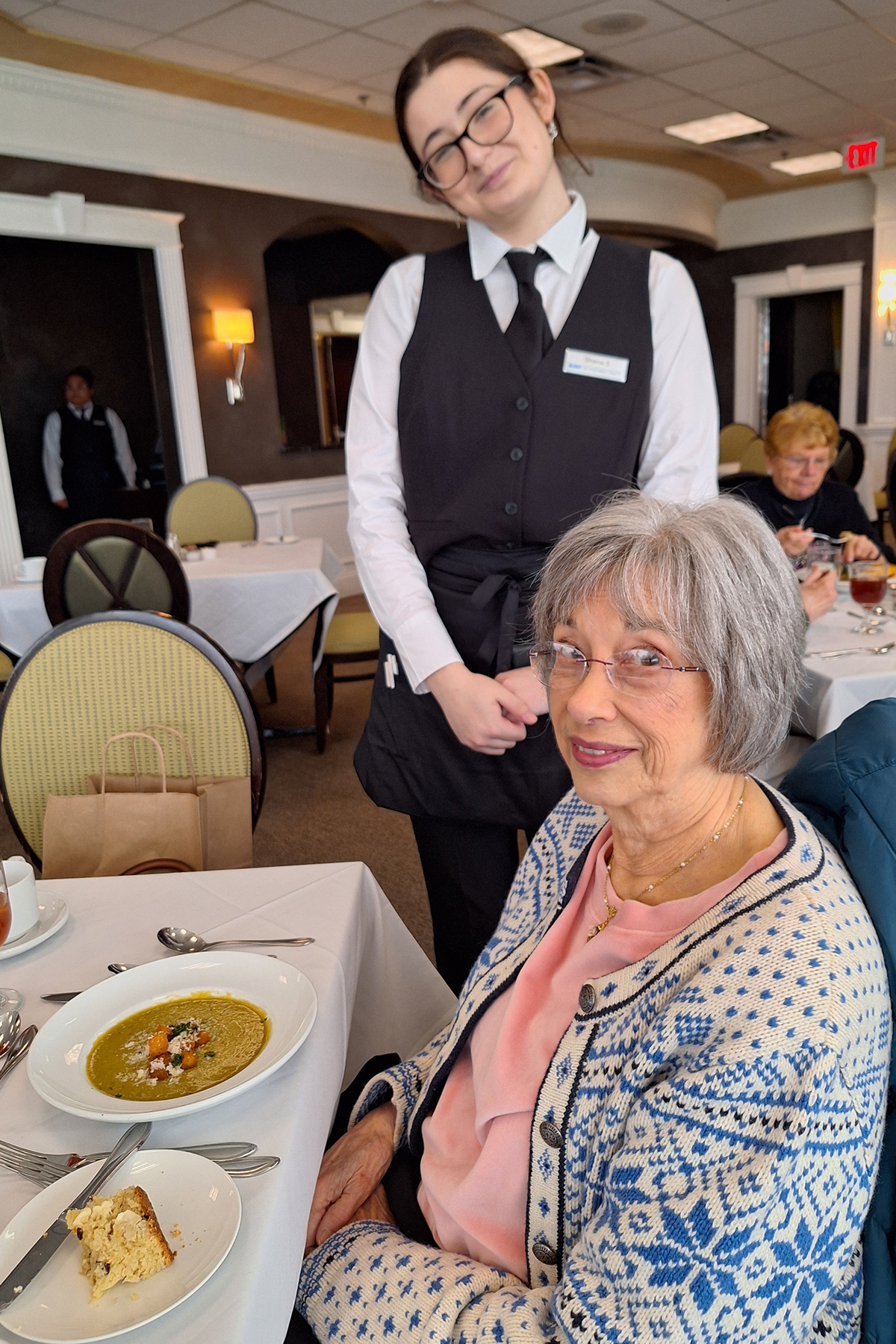 Student standing at table of patron in Casola Dining Room