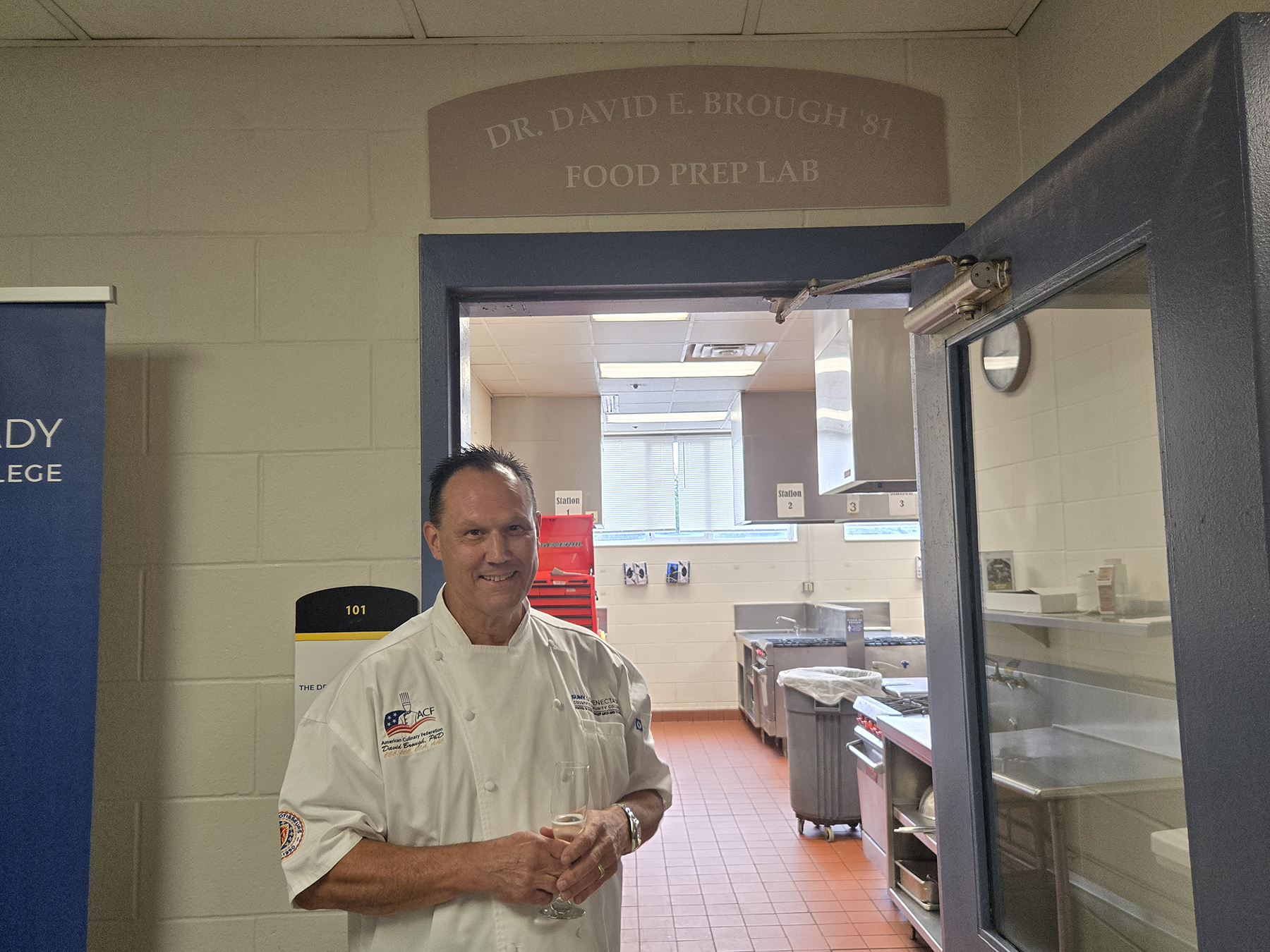 Dr. David Brough standing in front of Culinary Arts lab named for him