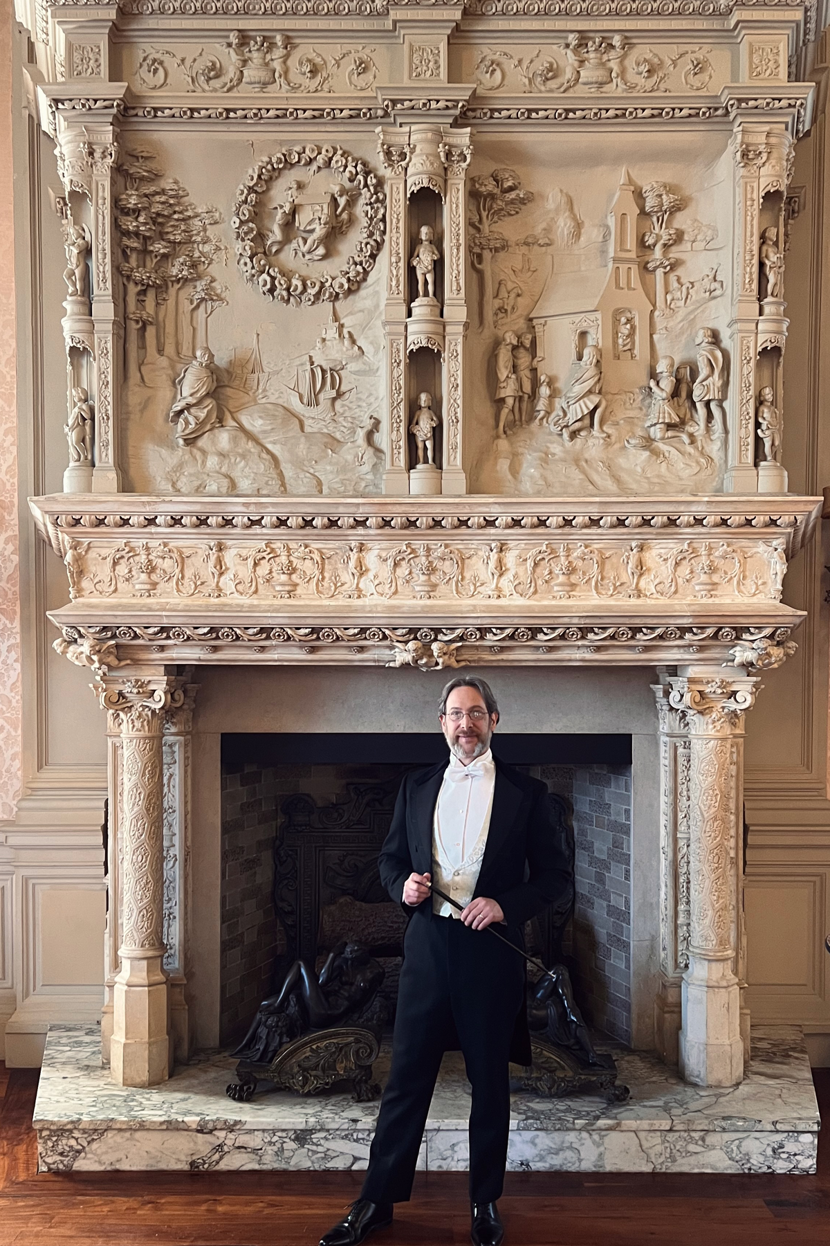 Dr. Brellochs in tuxedo standing in front of ornate fireplace in Rosecliff