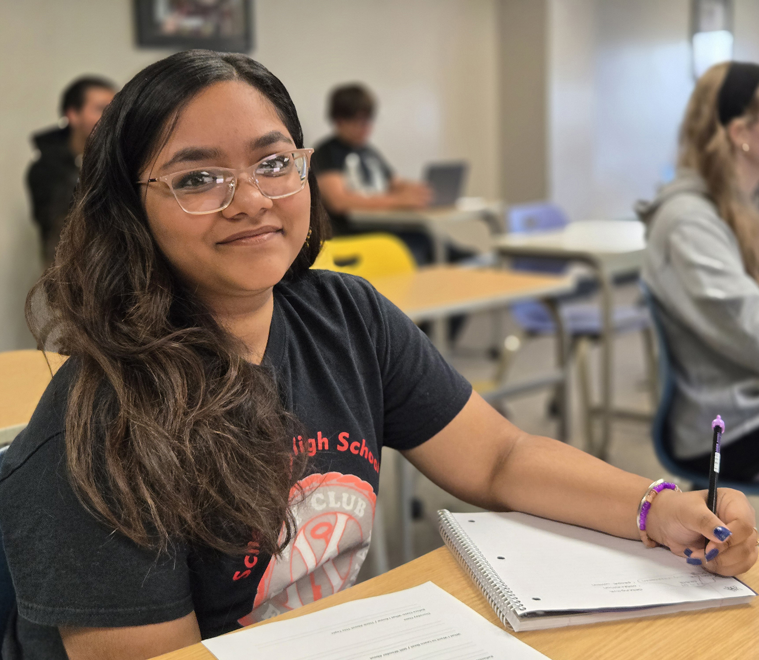 Student sitting in class, smiling at camera