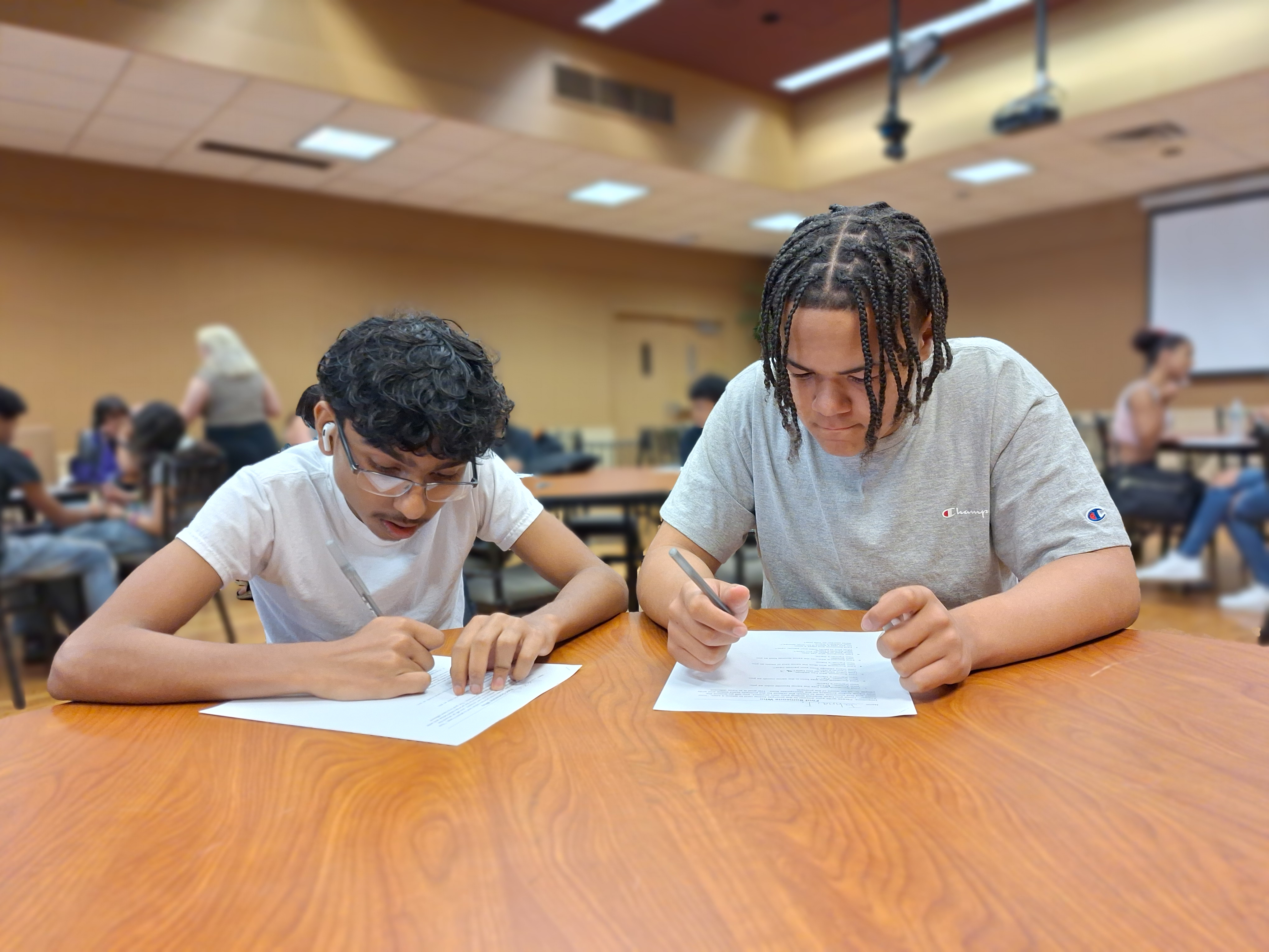 Two students writing on paper at table