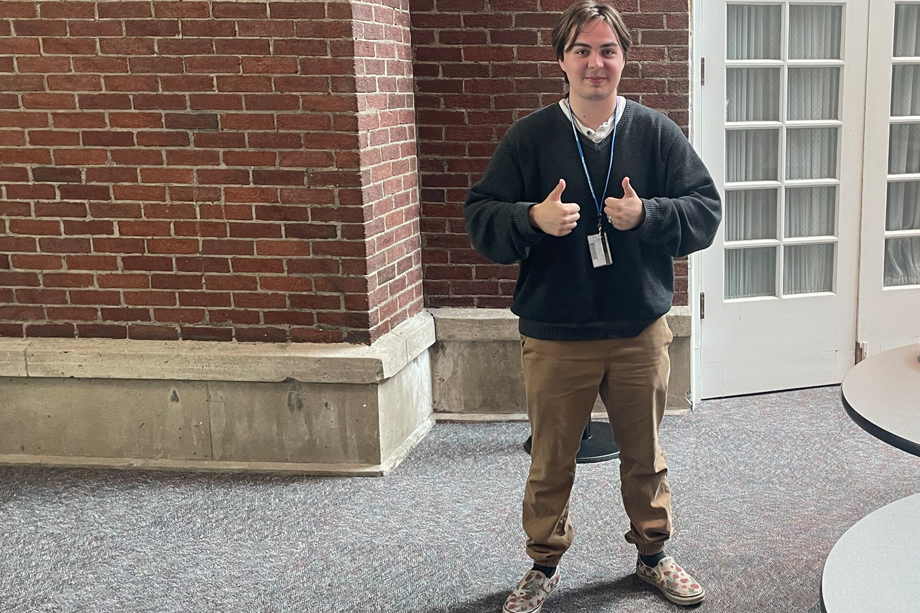 Elijah West standing in front of brick wall on campus, smiliing, thumbs up