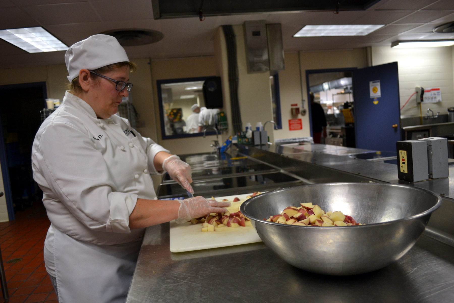 Kathy Darmetko in Culinary uniform in Culinary Arts lab cutting potatoes