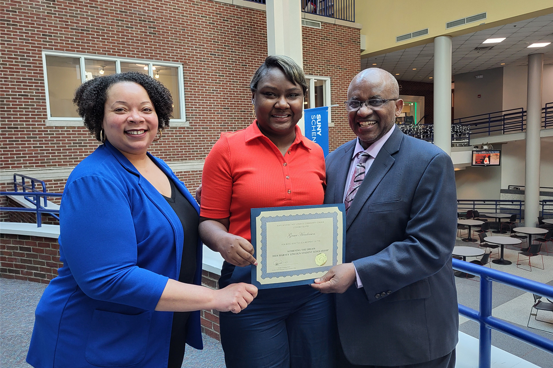 Grace Henderson holding scholarship certificate, standing in Elston Hall, with Dr. Moono and Tiombe Tatum