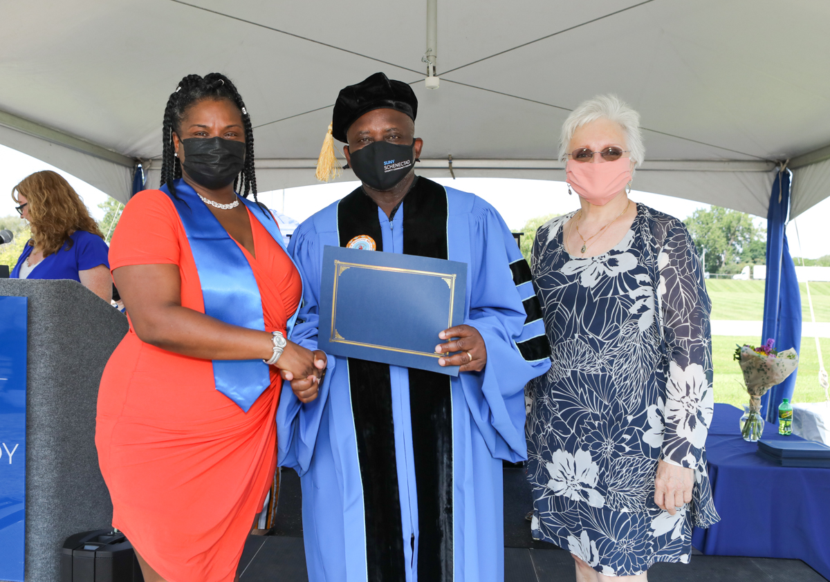 Healthcare Graduate Holding her certificate with Dr. Moono and Dr. Rota on stage