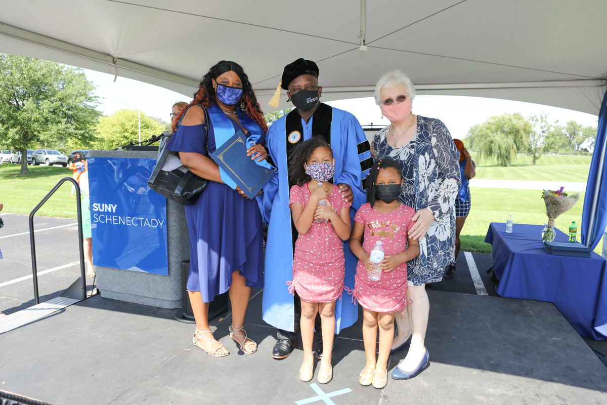 Healthcare grad and her children on stage with Dr. Moono and Dr. Rota