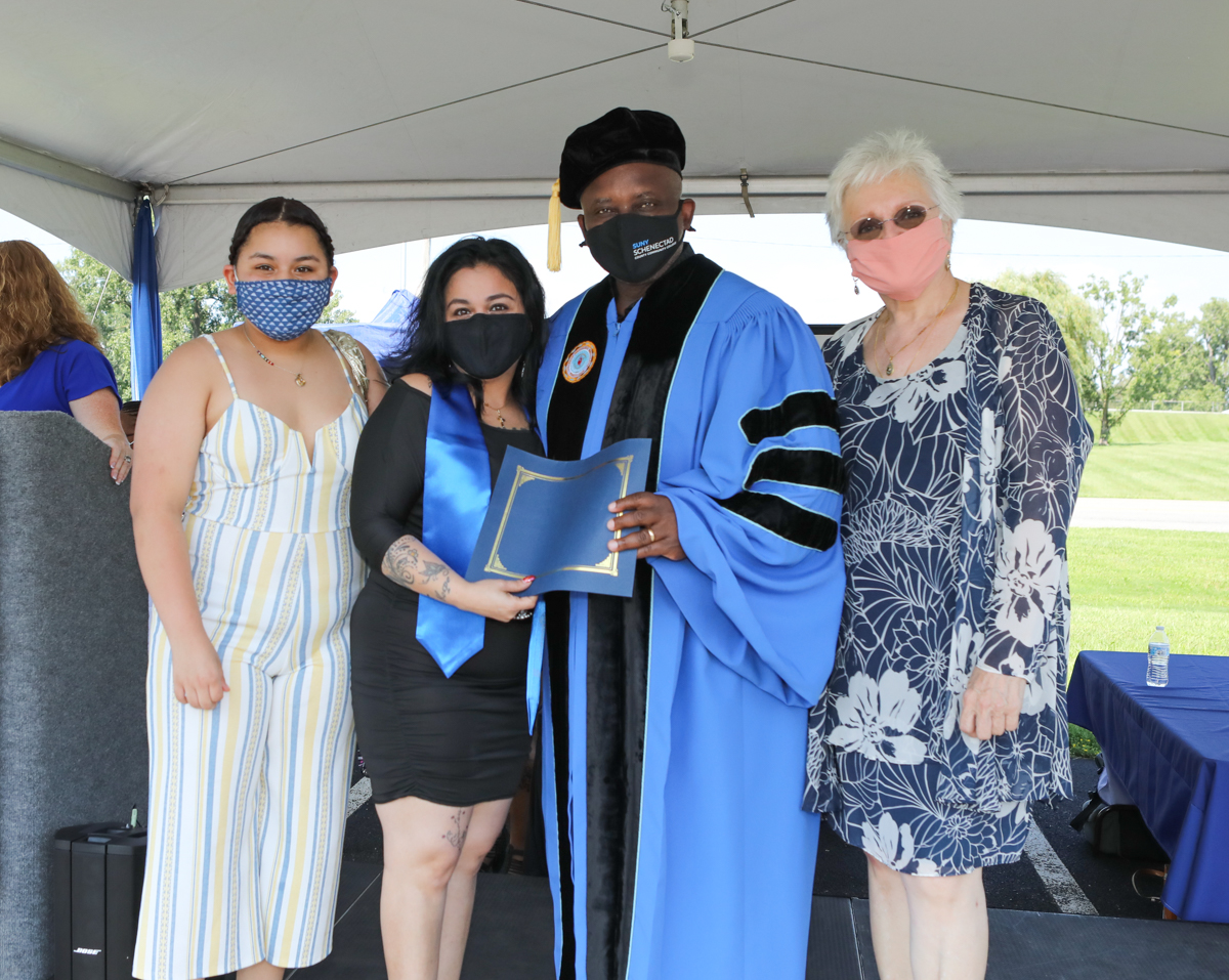 Healthcare grad and children on stage with Dr. Moono and Dr. Rota