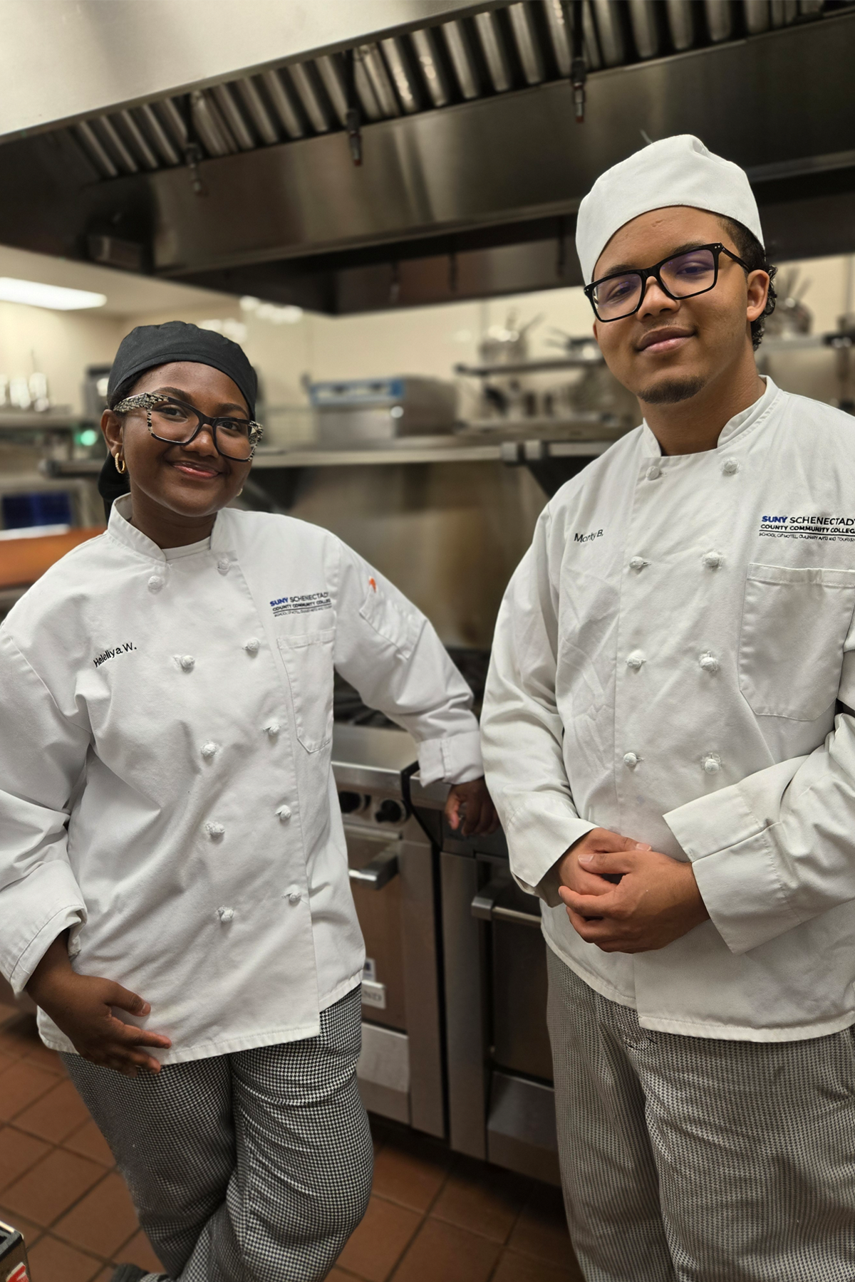 Haleliya Wilson and Monty Belfort, wearing chef's uniforms, standing in culinary arts kitchen