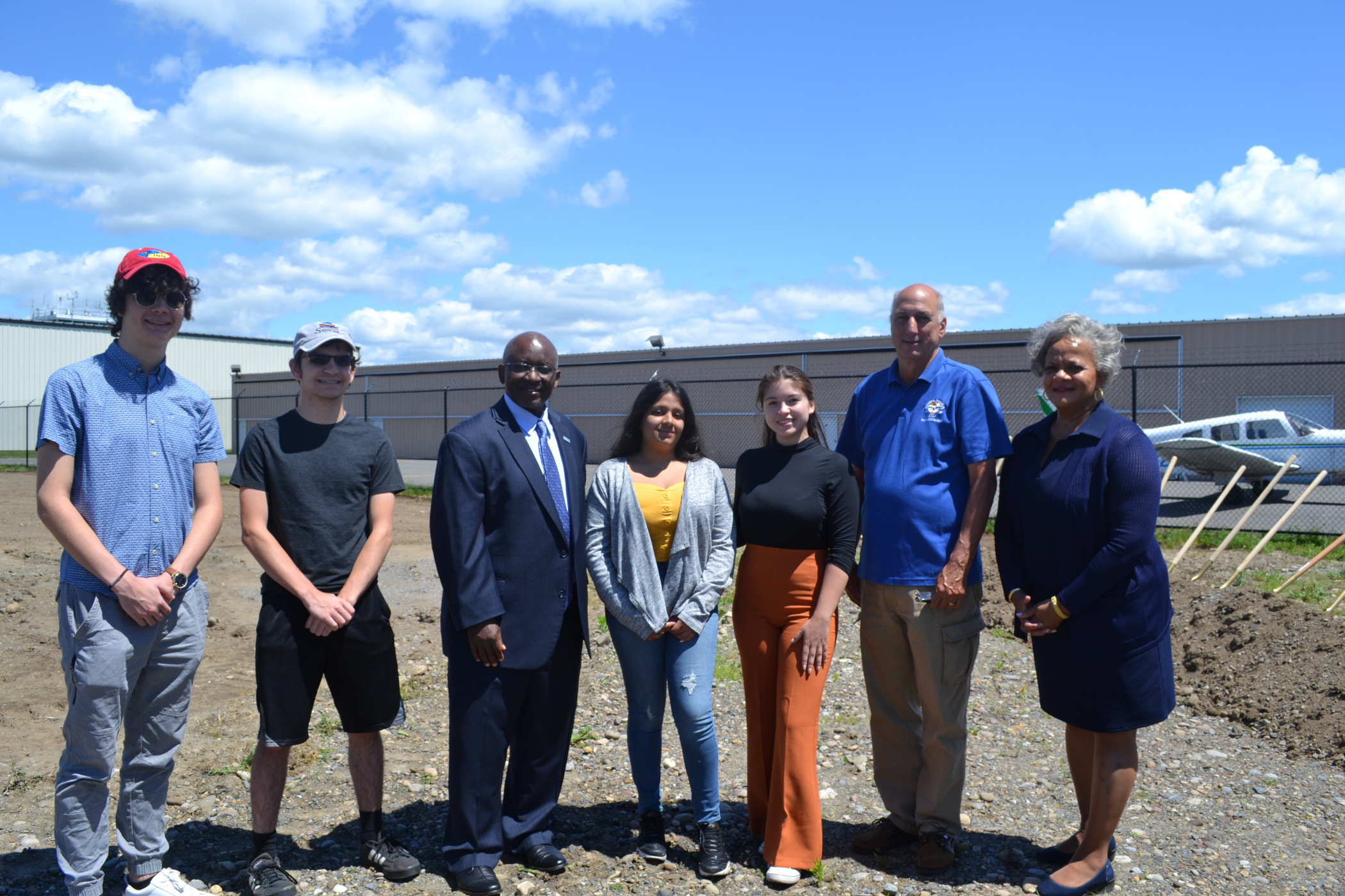 College faculty and students standing in front of construction space where hangar will be located