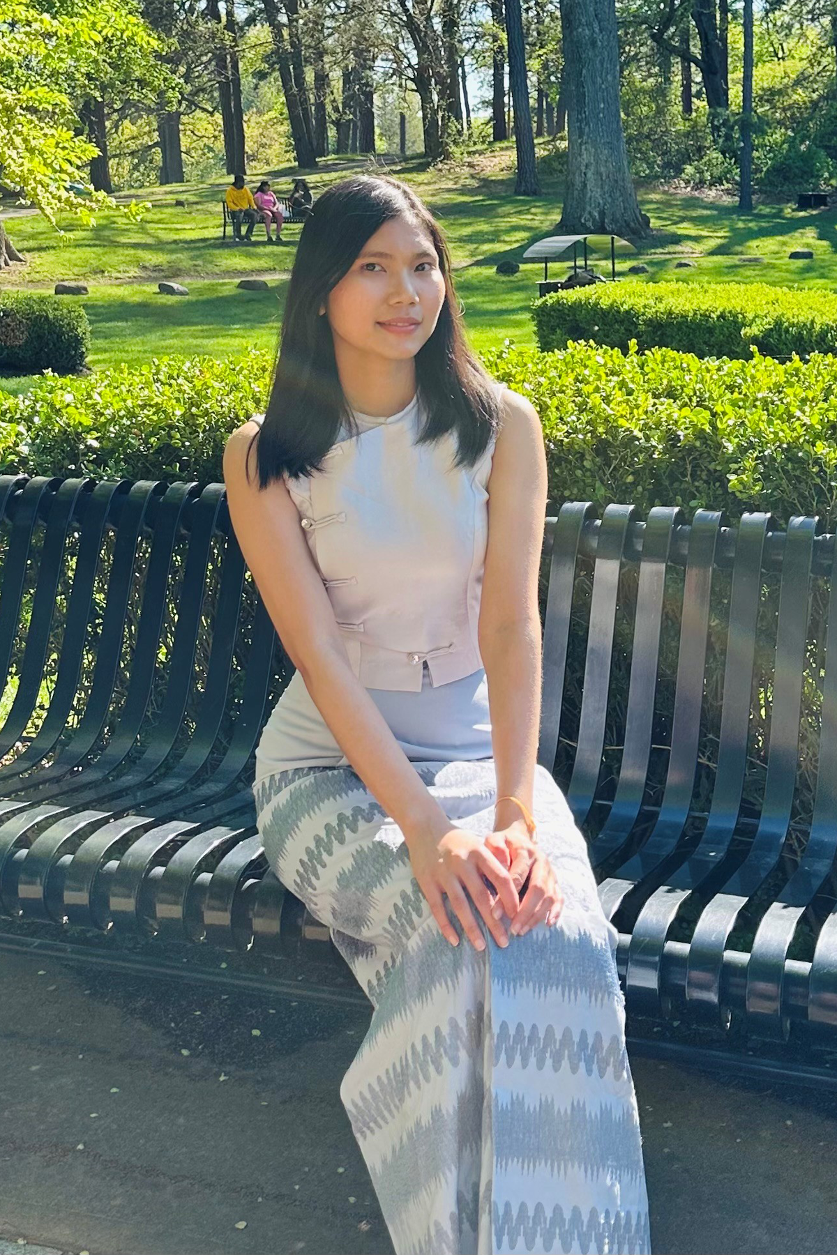 Hsu Win sitting on a bench outside, green grass behind her