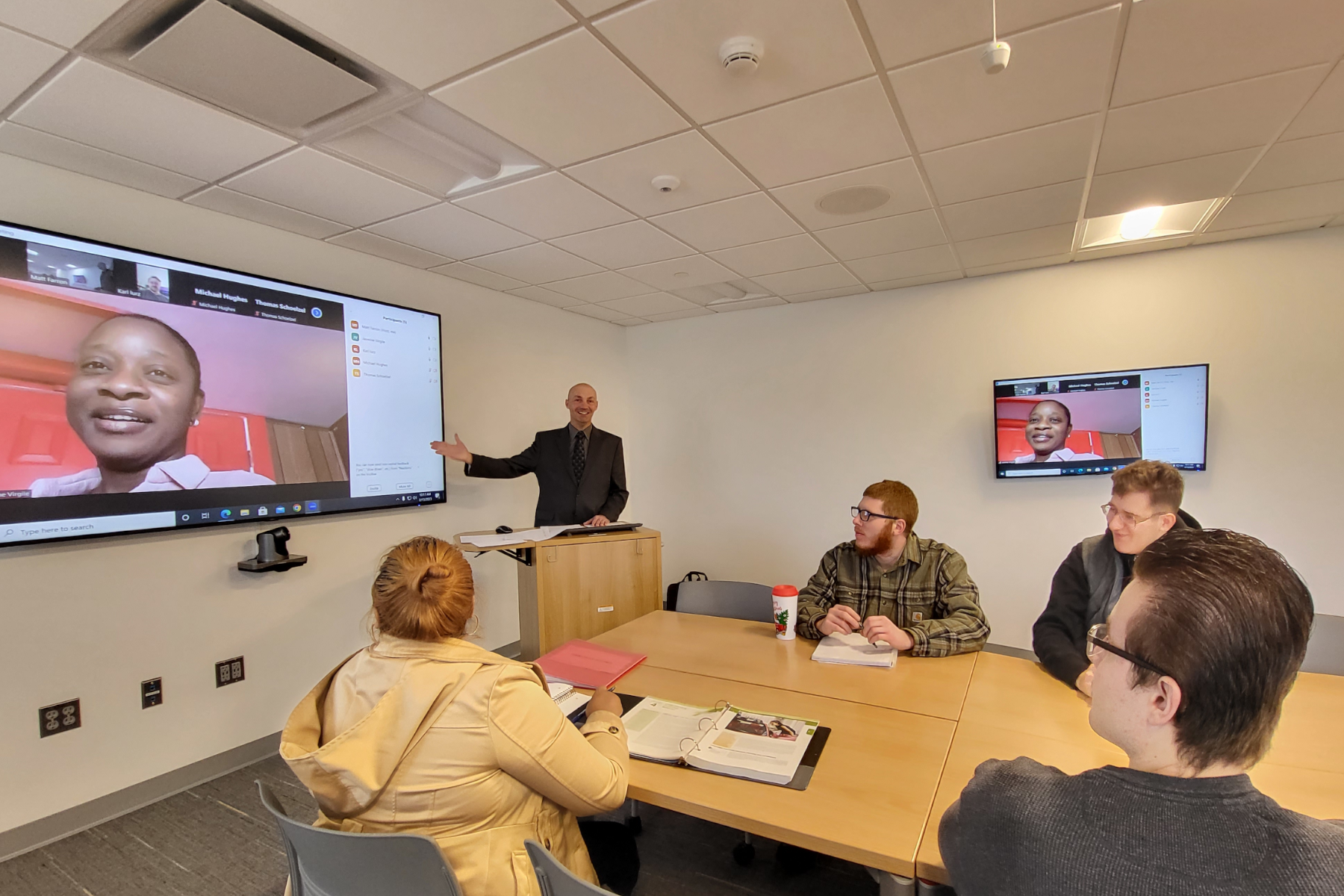 Students in classroom with Professor Matt Farron and students on video on large screen at front of classroom