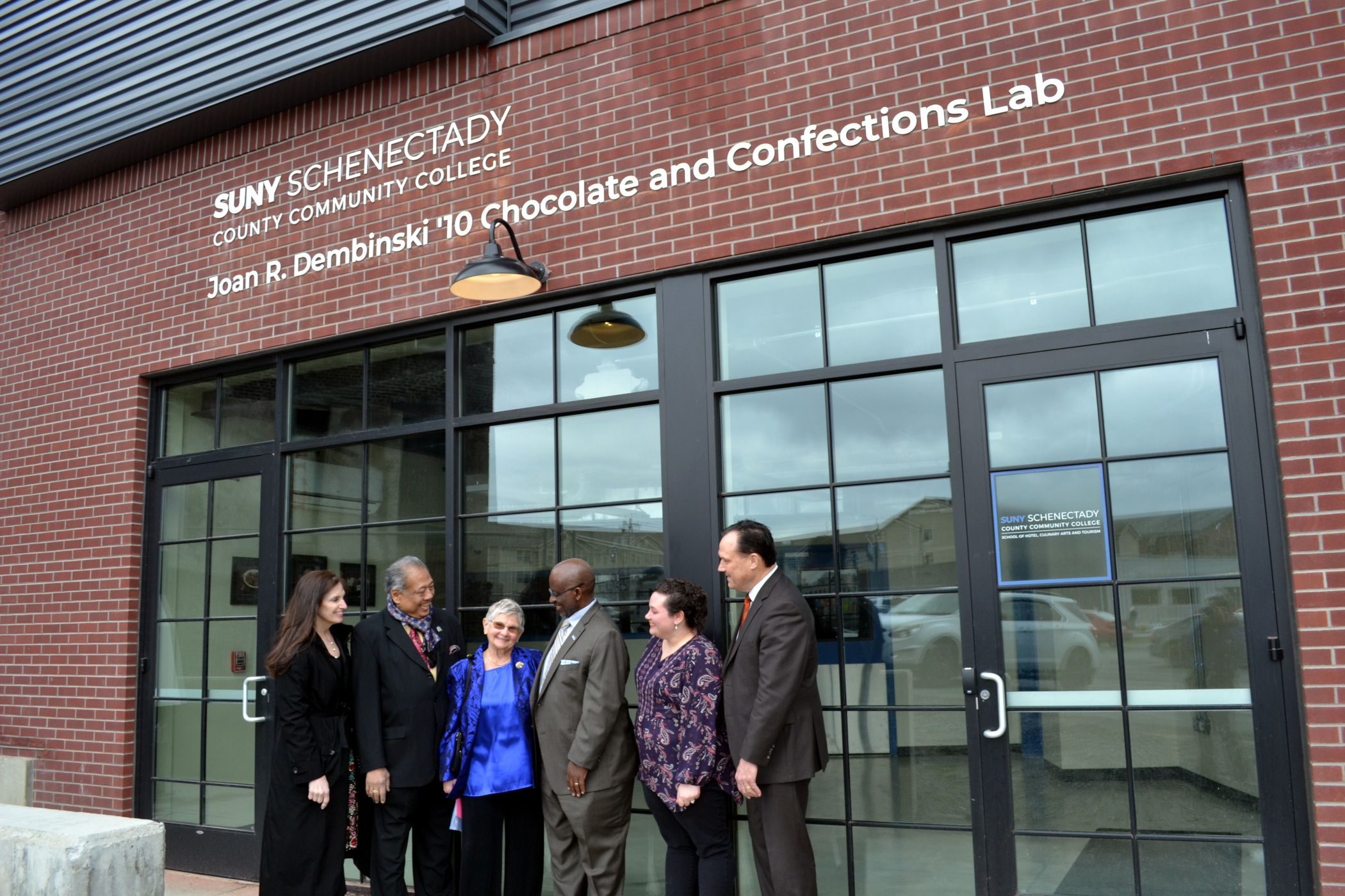 Joan Dembinski and college officials standing outside lab with her name on building