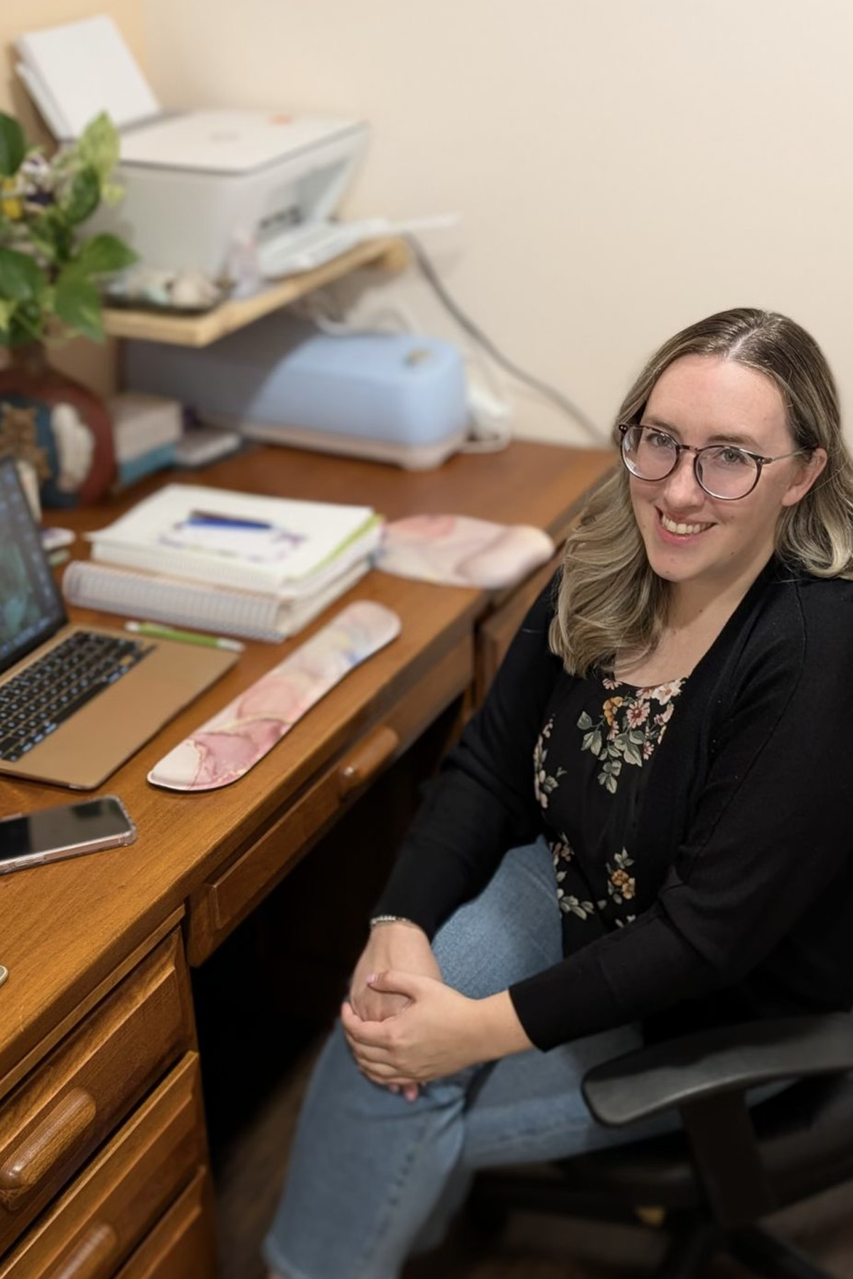 Alumna Karly Zepf smiling, sitting at her desk, in front of her laptop 