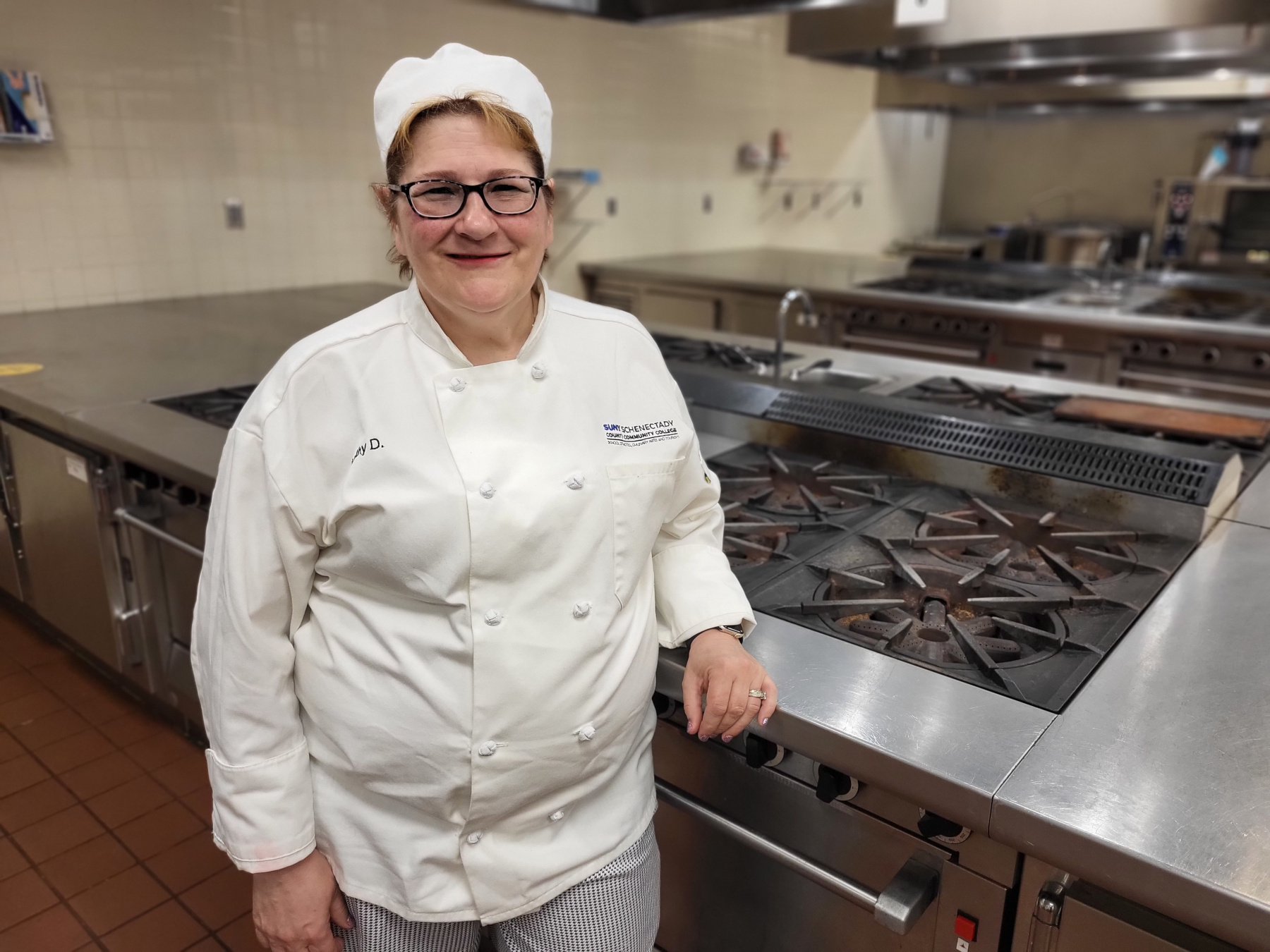 Kathy Duffy-Darmetko standing near stove in Culinary Arts Lab, smiling