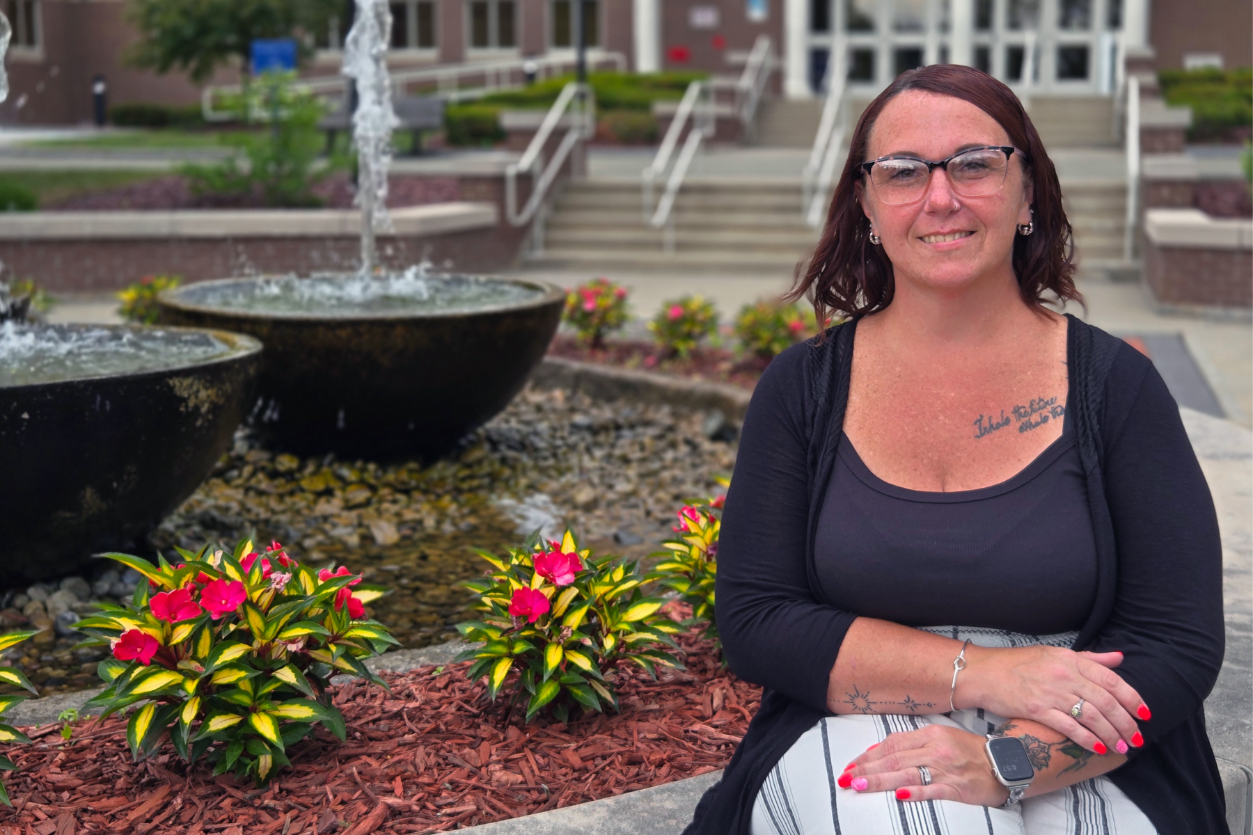 Kristina Waters, sitting outside near fountain, smiling, flowers in the background