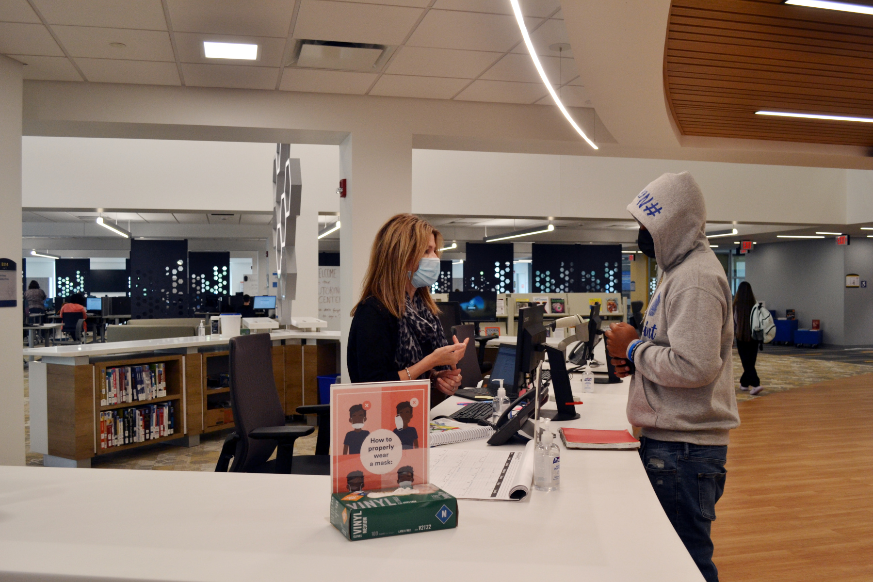 Librarian assisting student standing at reference desk