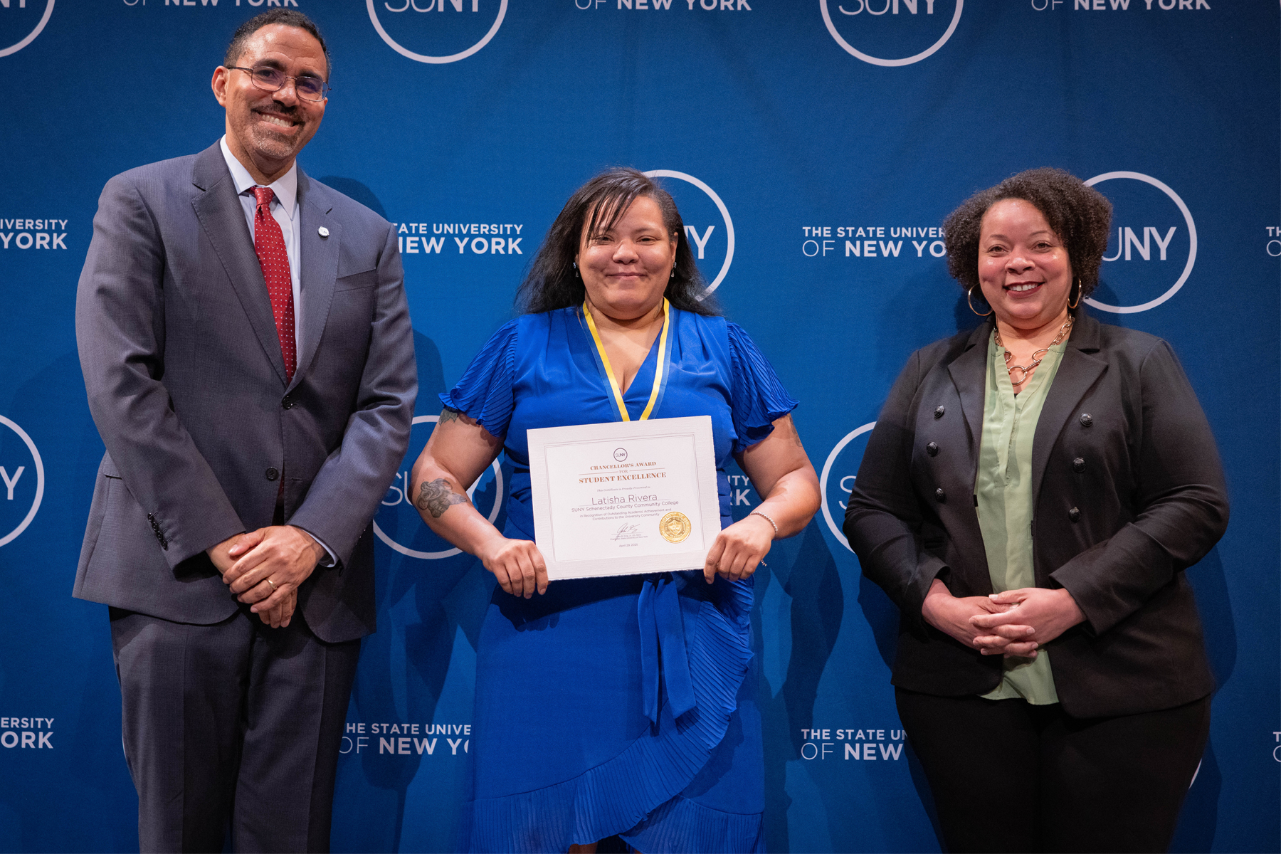 Latasha Rivera, smiling, holding certificate, with SUNY Chancellor John B. King Jr. and Tiombe Farley