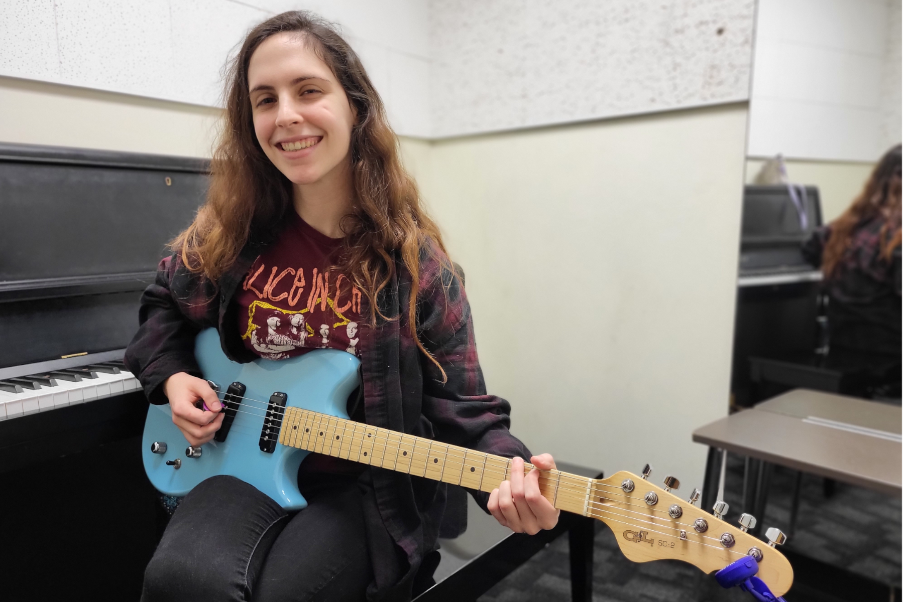 Layla Burkhouse seated in music practice room, playing electric guitar