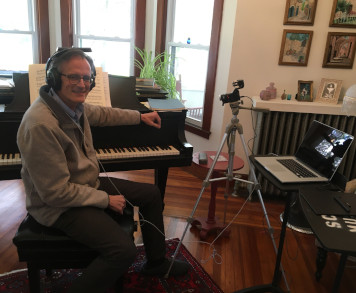 Pianist Mark Evans with headphones on seated at piano in home music studio