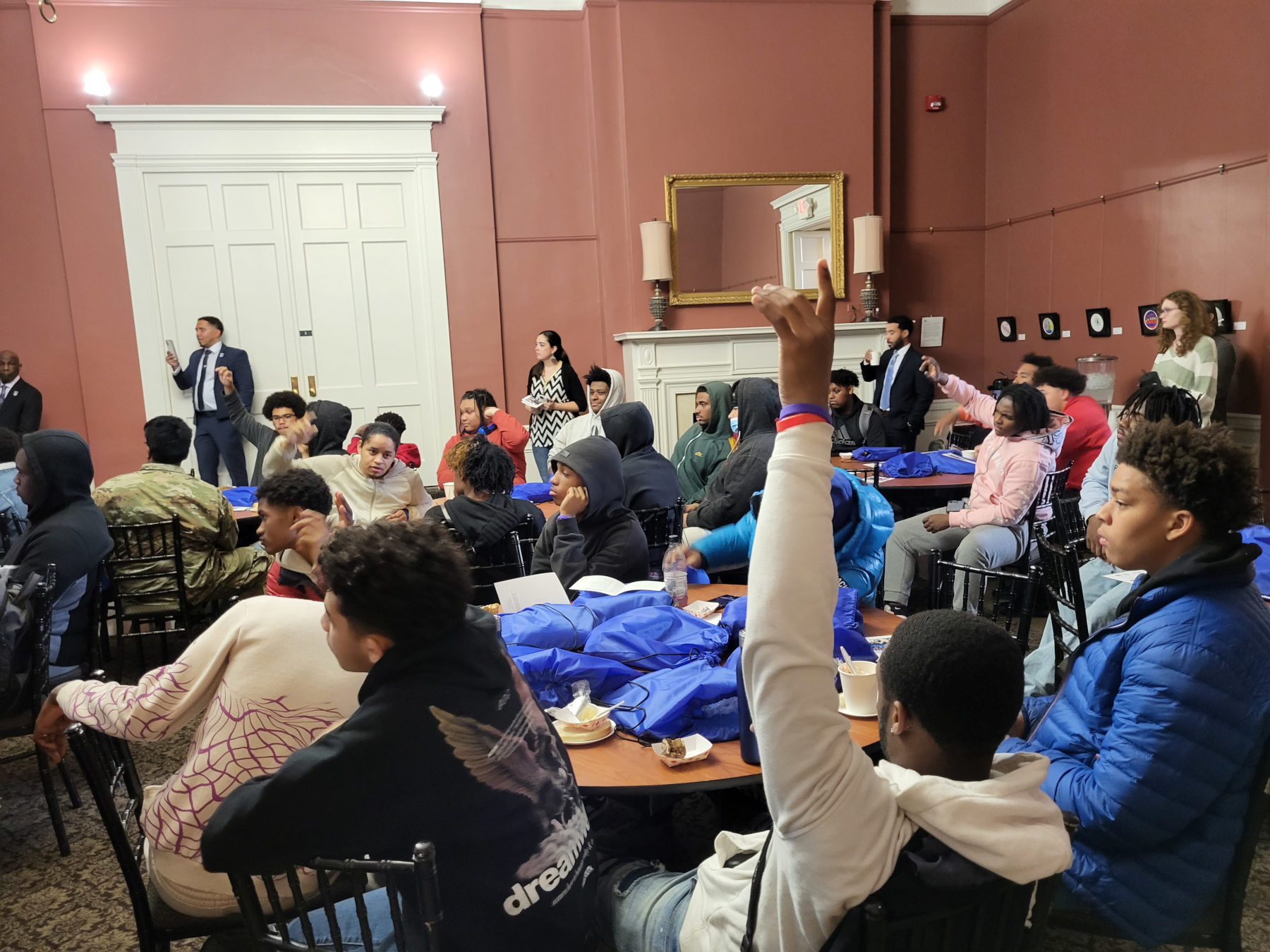 Students seated at tables, raising their hands