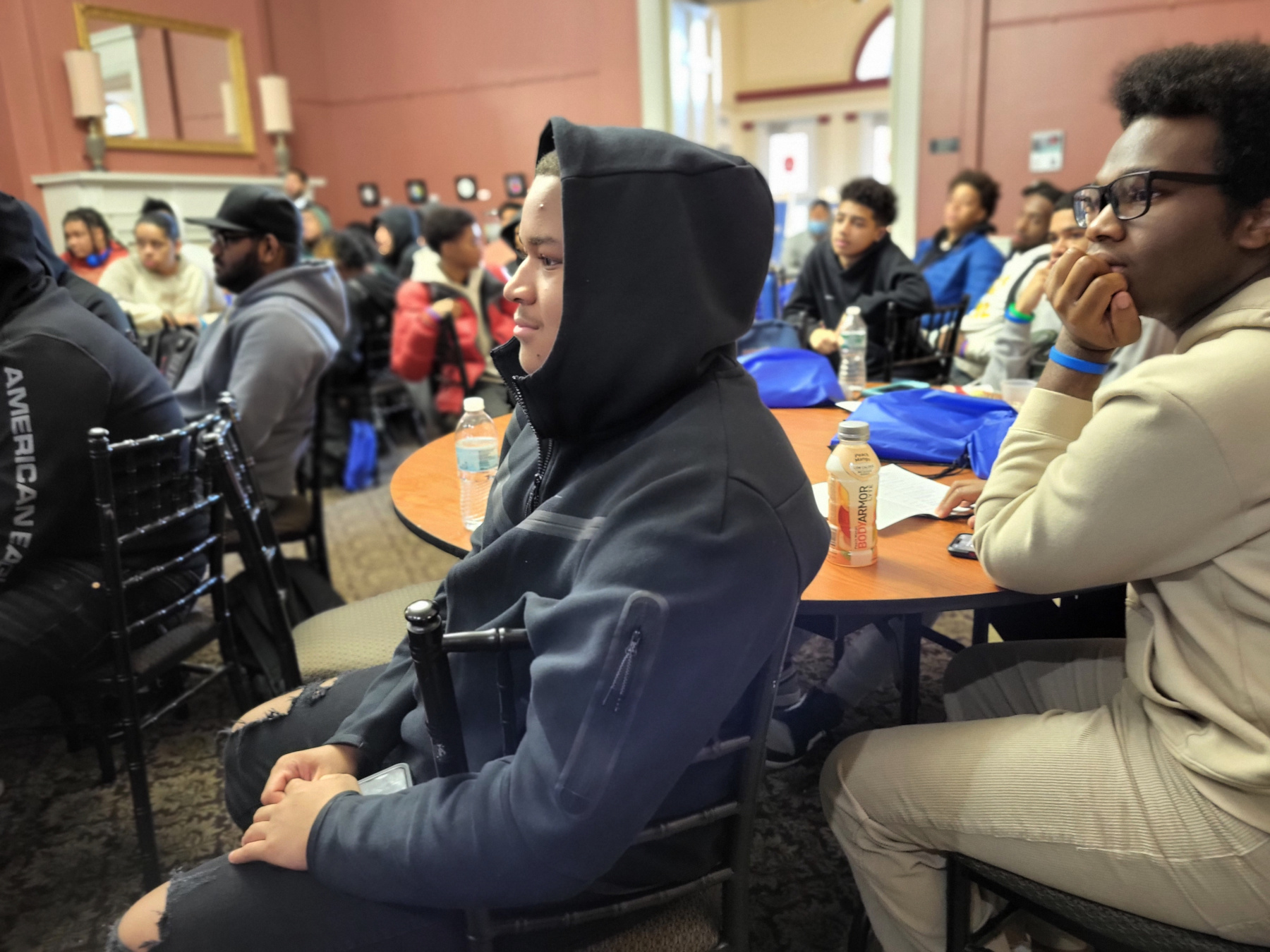 Schenectady high School students Jayden Birch and Arnaud West seated at table, listening to Dr. Moono speaking.