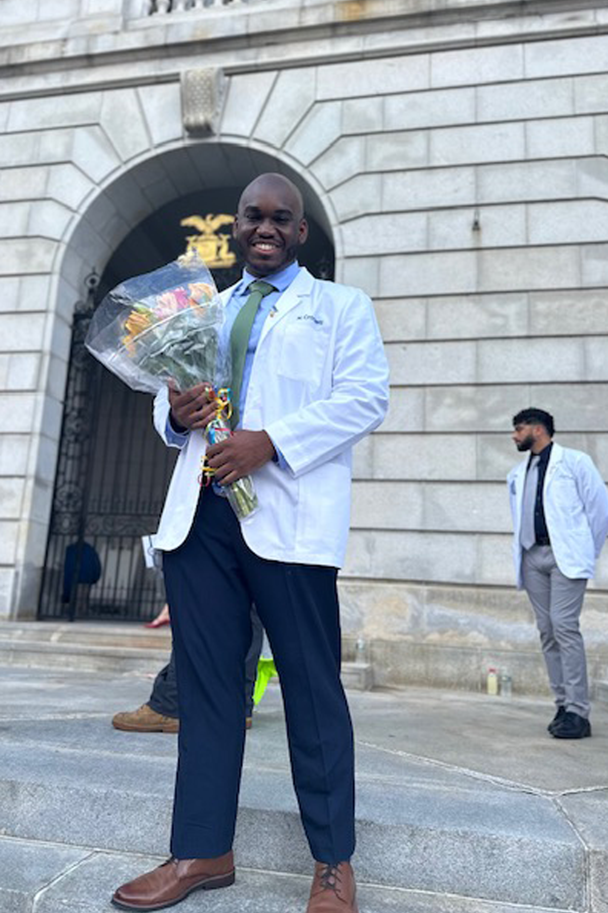 Nieem Crockett in his white coat, holding flowers, standing outside