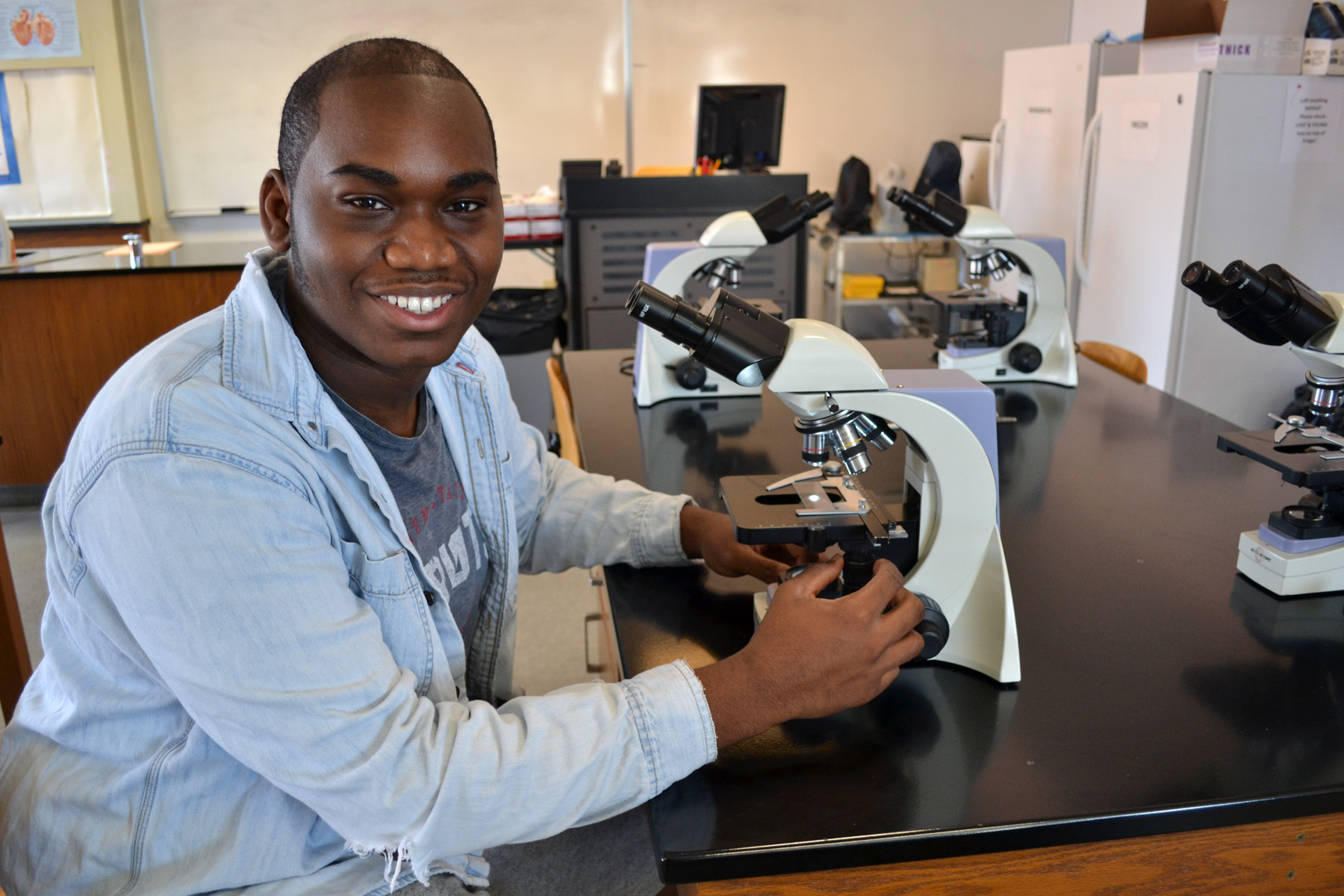 Nieem Crockett sitting and looking at microscope in Biology Lab