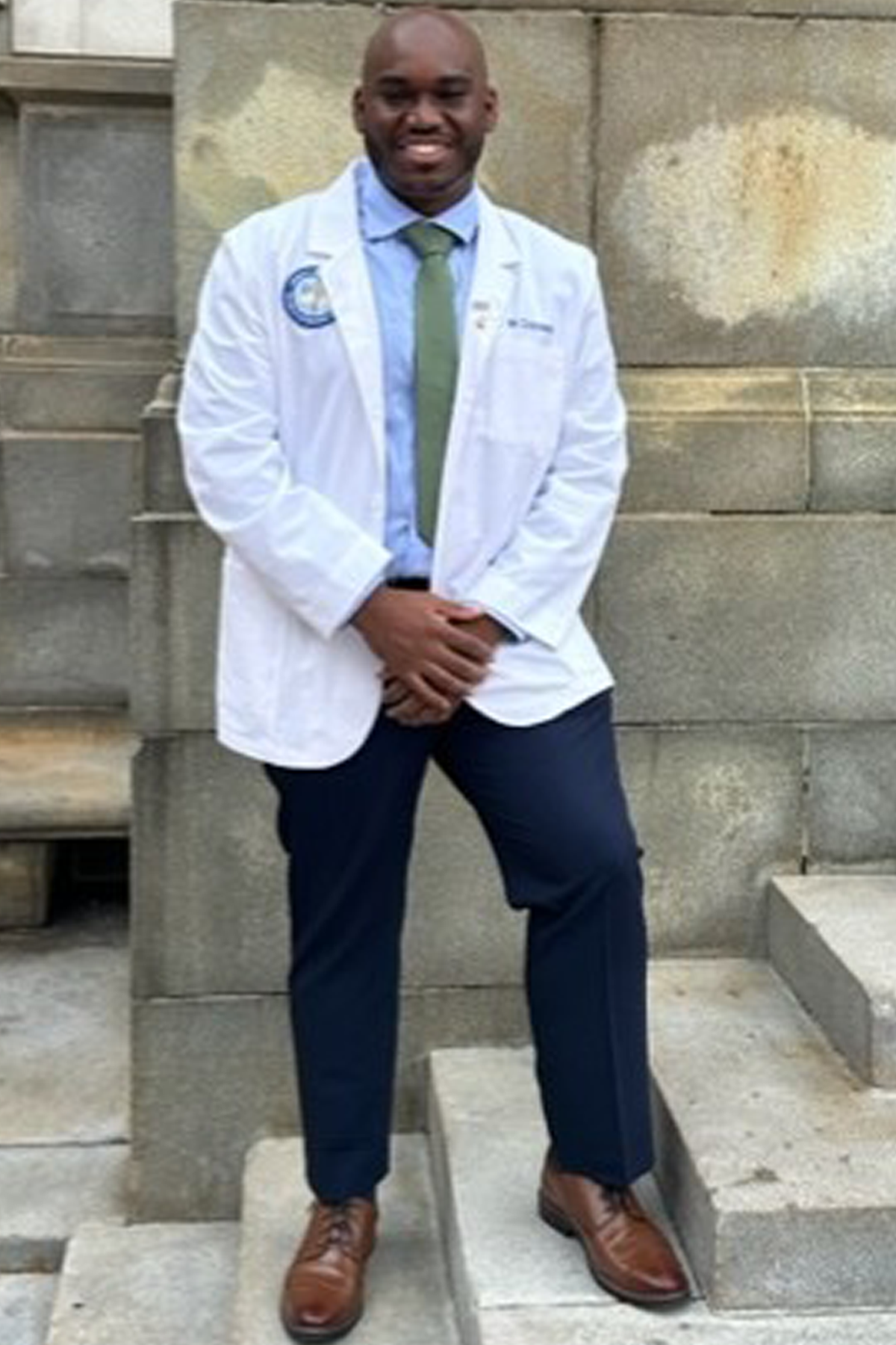 Nieem Crockett in white coat, standing on the steps outside