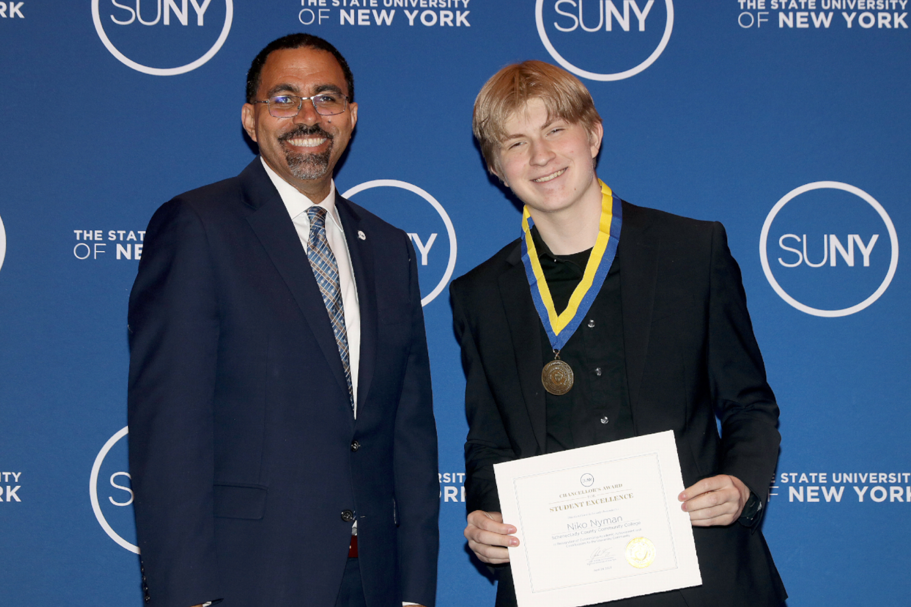 SUNY Chancellor John B. King Jr. standing with Niko Nyman, smiling in front of SUNY backdrop