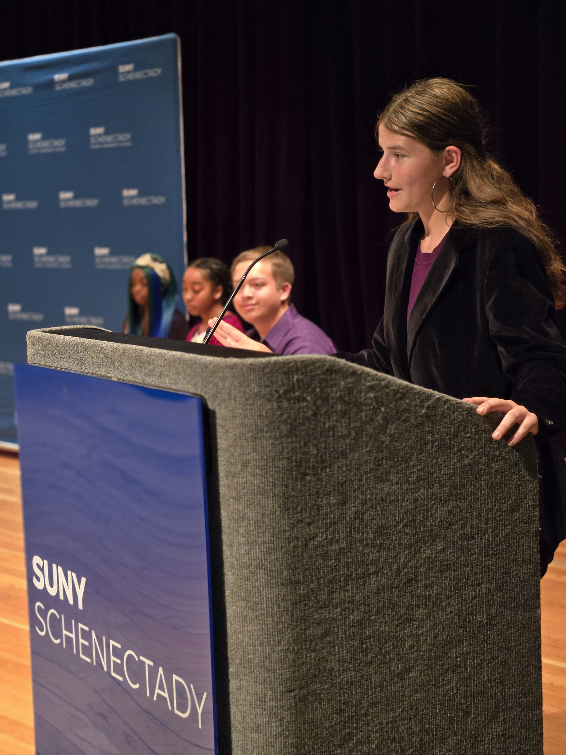 Grace VanBaaren speaking at podium on stage