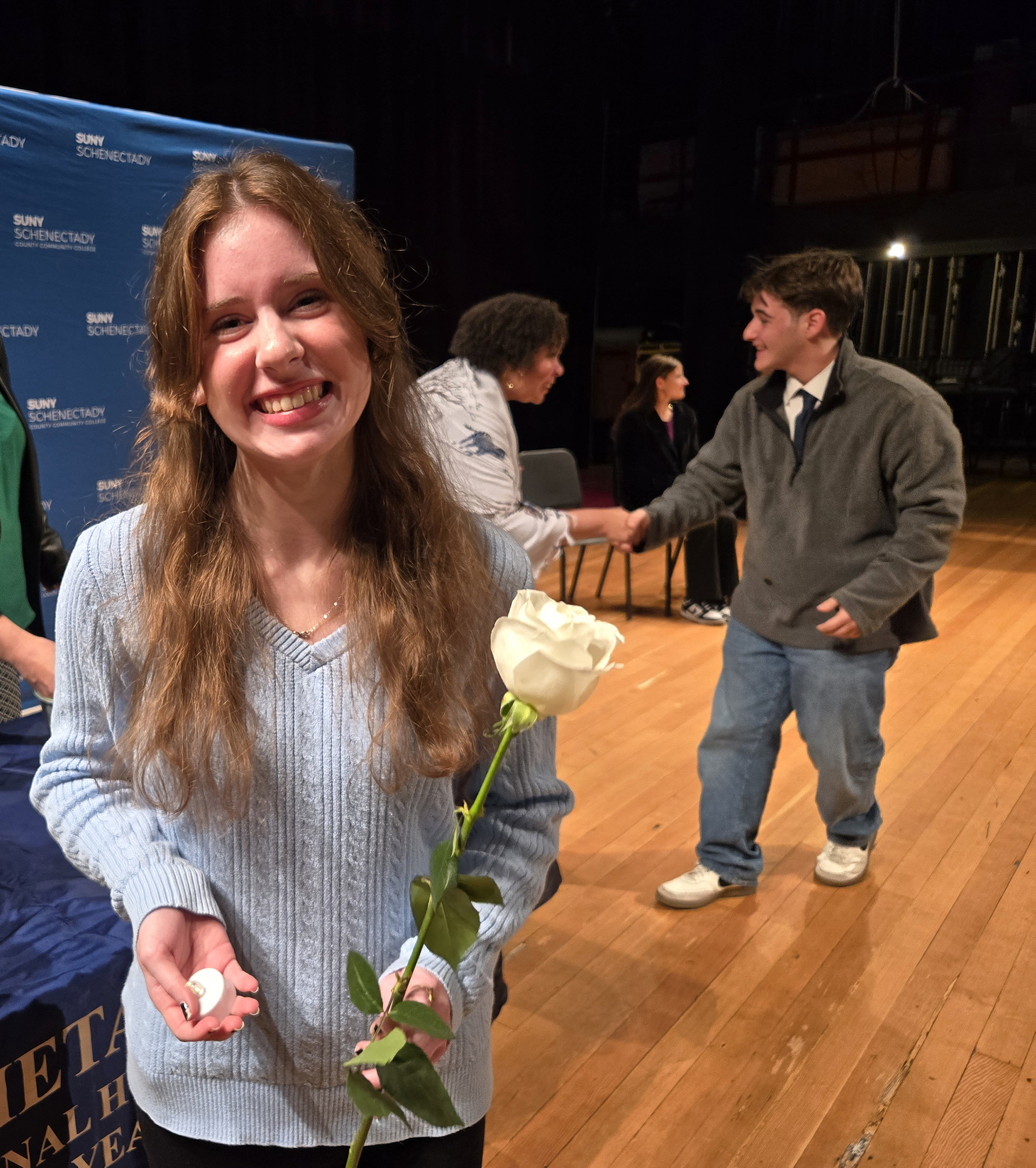 Student on stage holding white rose