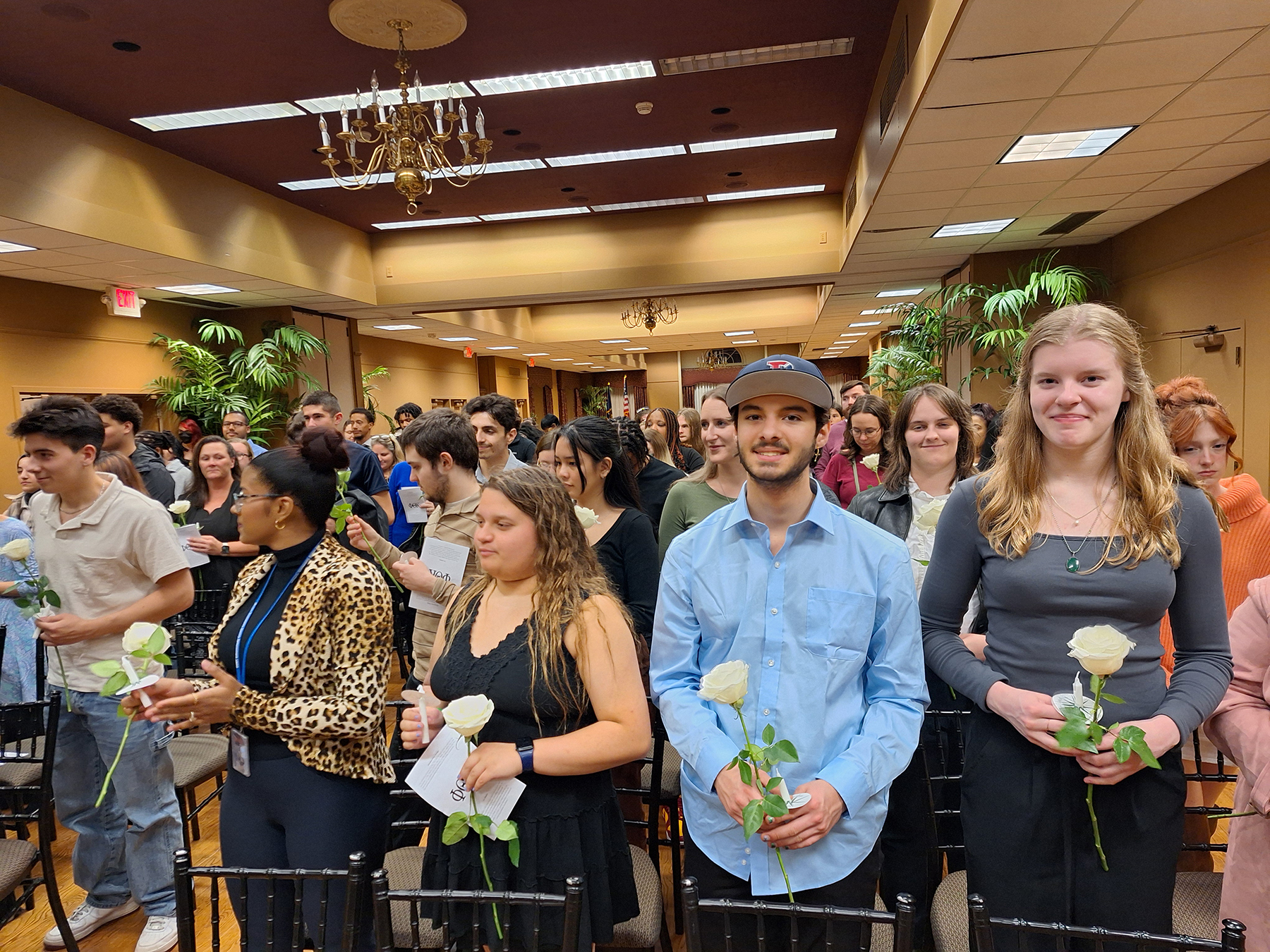 Student standing in rows, holding white roses, smiling